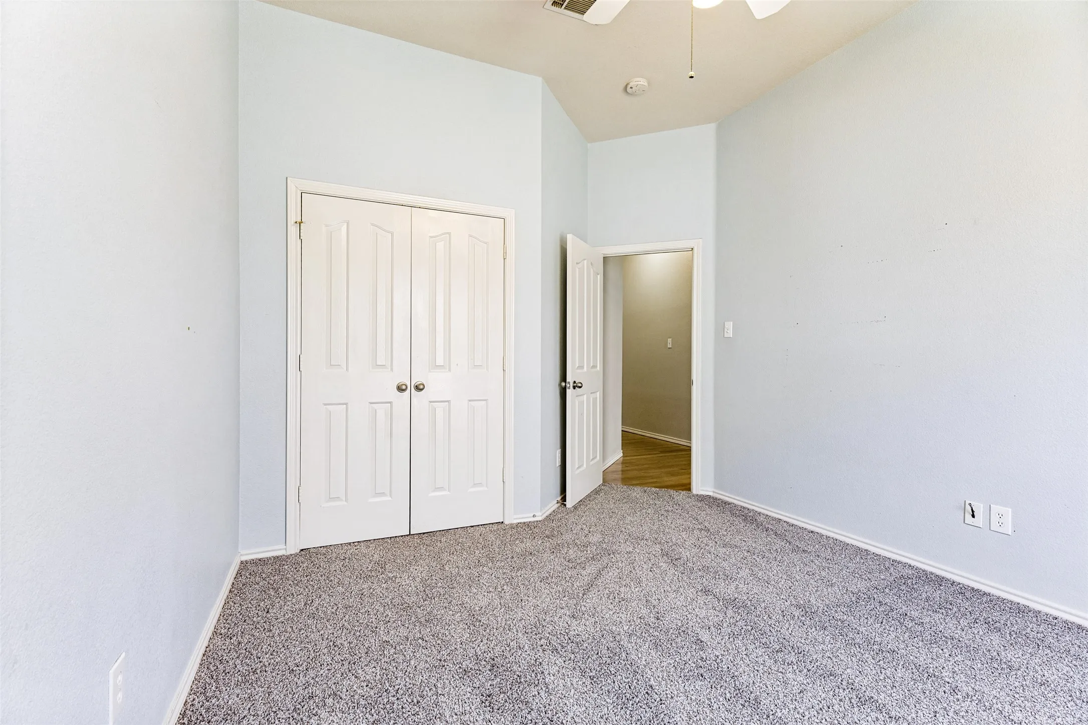 Vaulted ceiling bedroom featuring plush gray carpet, a ceiling fan, and double panel closet doors