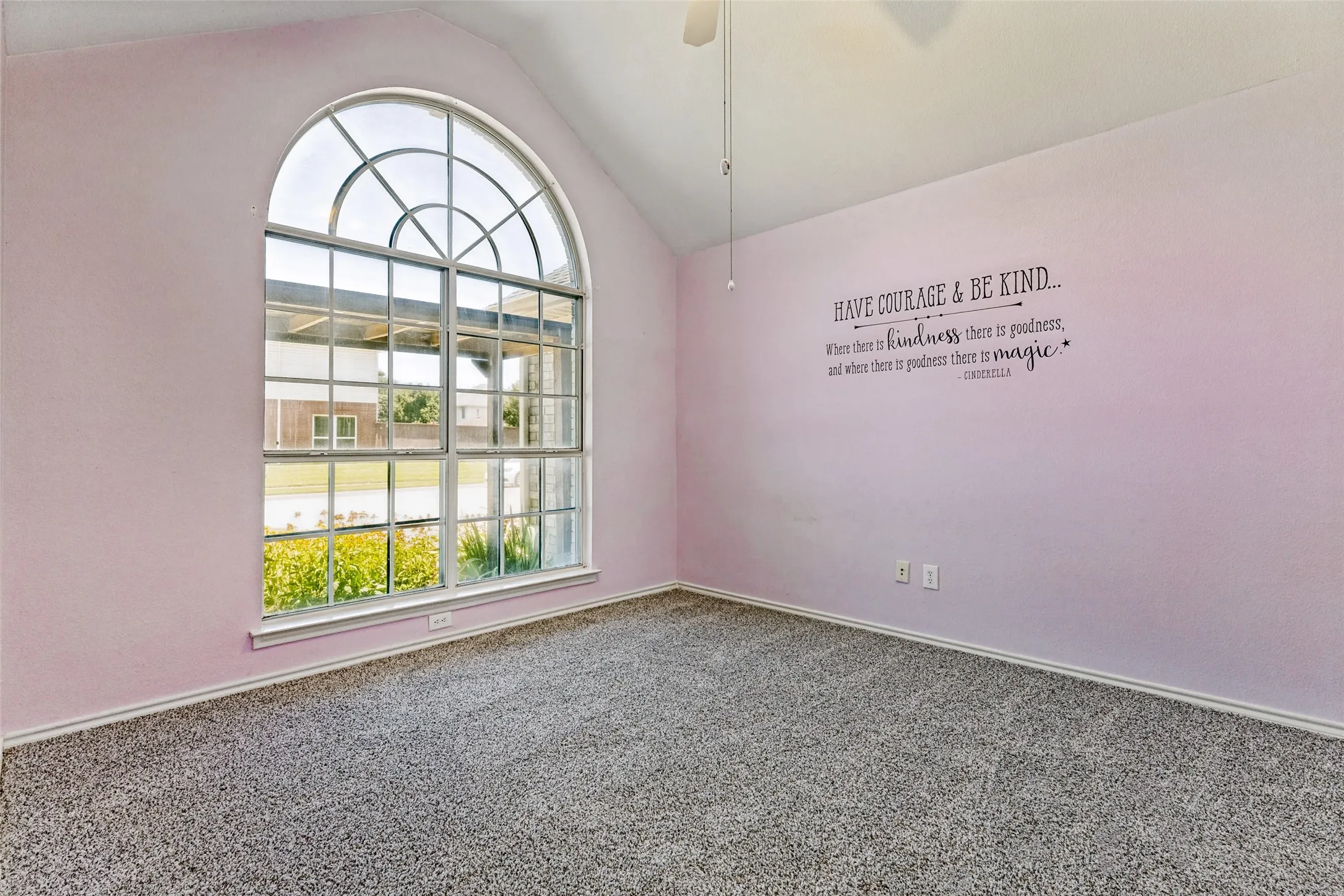 Vaulted ceiling room featuring an expansive arched window with grid details, light gray carpet flooring, and a ceiling fan