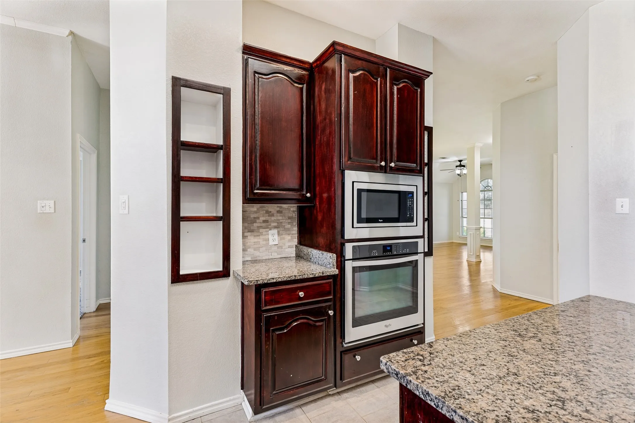 Built-in stainless steel microwave and oven combination with dark wood-finish cabinetry, granite countertops, and a tiled backsplash