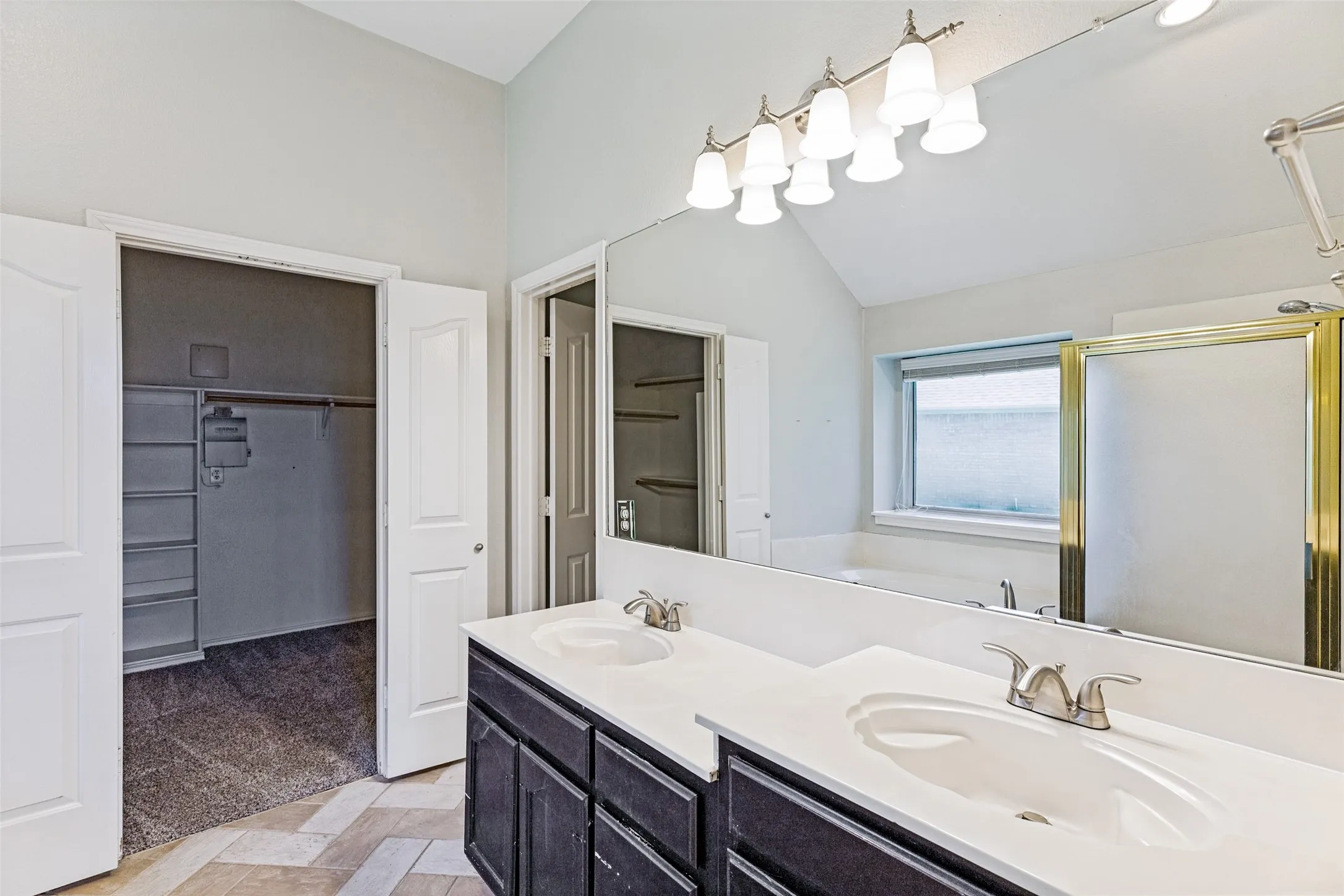 Bathroom featuring dual sinks with white countertops, dark wood-finish cabinetry, and a large wall-mounted mirror