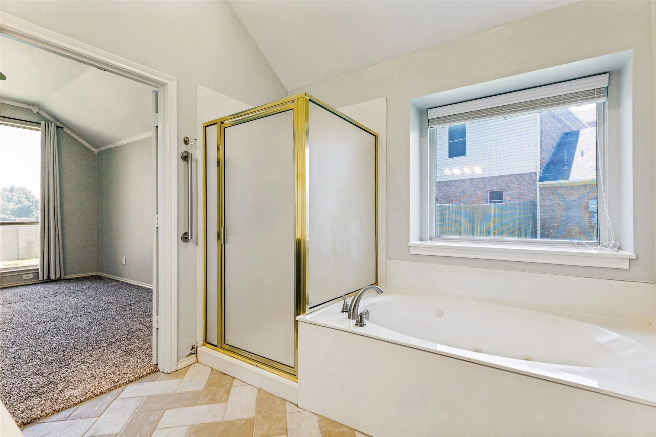 Bathroom featuring a built-in jetted tub, a frosted glass and brass-tone shower enclosure, and herringbone-patterned floor tiles