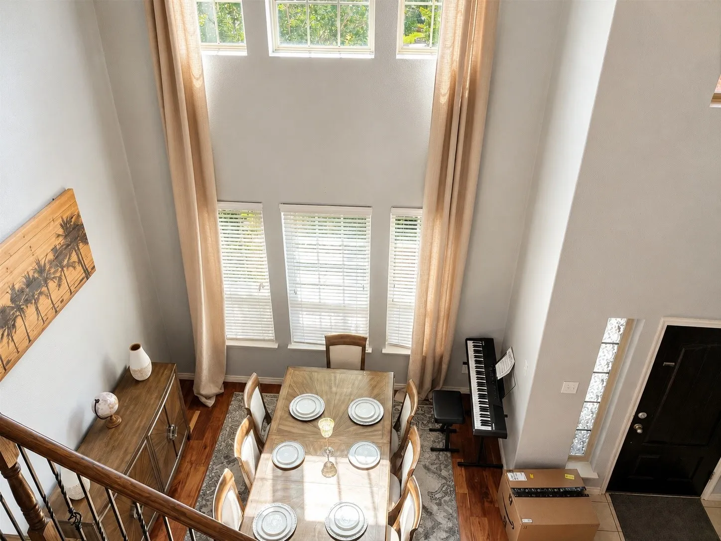 Two-story living area featuring multiple windows with blinds, hardwood flooring, and a dark wood staircase with black metal balusters