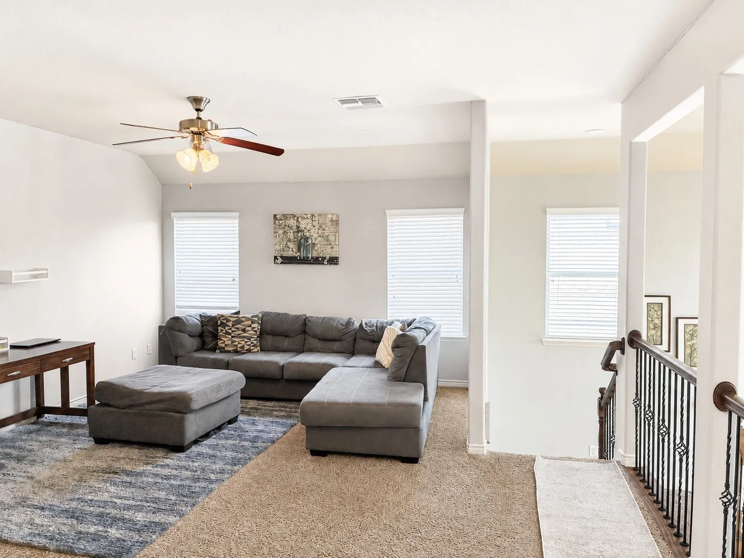 Carpeted living area featuring multiple windows, a ceiling fan with integrated lighting, and a console table