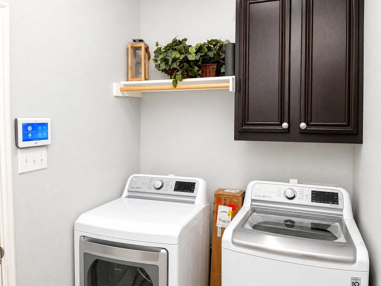 Dedicated laundry space featuring dark wood-finish cabinetry with silver hardware, a white wall-mounted shelf with a wood-finish rod, and light gray wall paint