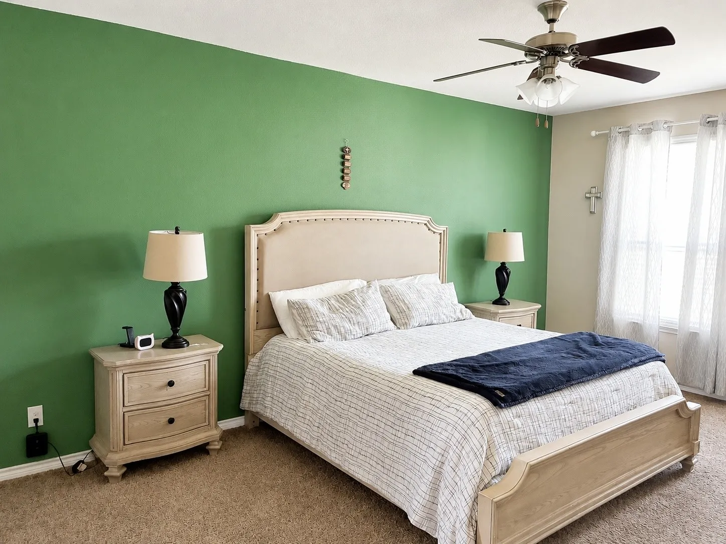 Plush carpet flooring, a ceiling fan with integrated lighting, and a large window with white sheer curtains