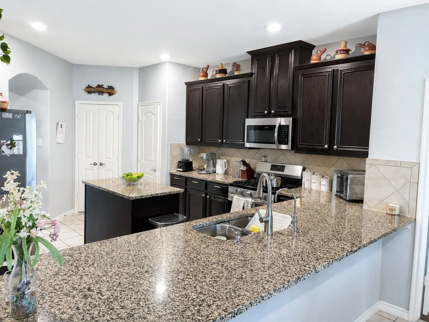 Kitchen featuring stone-finish countertops, dark wood cabinetry, a stainless steel microwave, and a stainless steel gas range