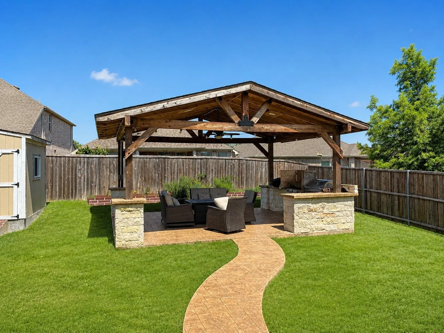 Expansive backyard featuring a covered outdoor kitchen, wood-beam pavilion, stamped concrete patio, and a storage shed