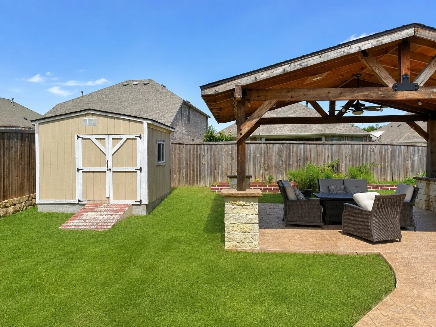 Expansive outdoor area featuring a substantial wood pergola with ceiling fan, stamped concrete patio, and a dedicated storage shed with a brick ramp