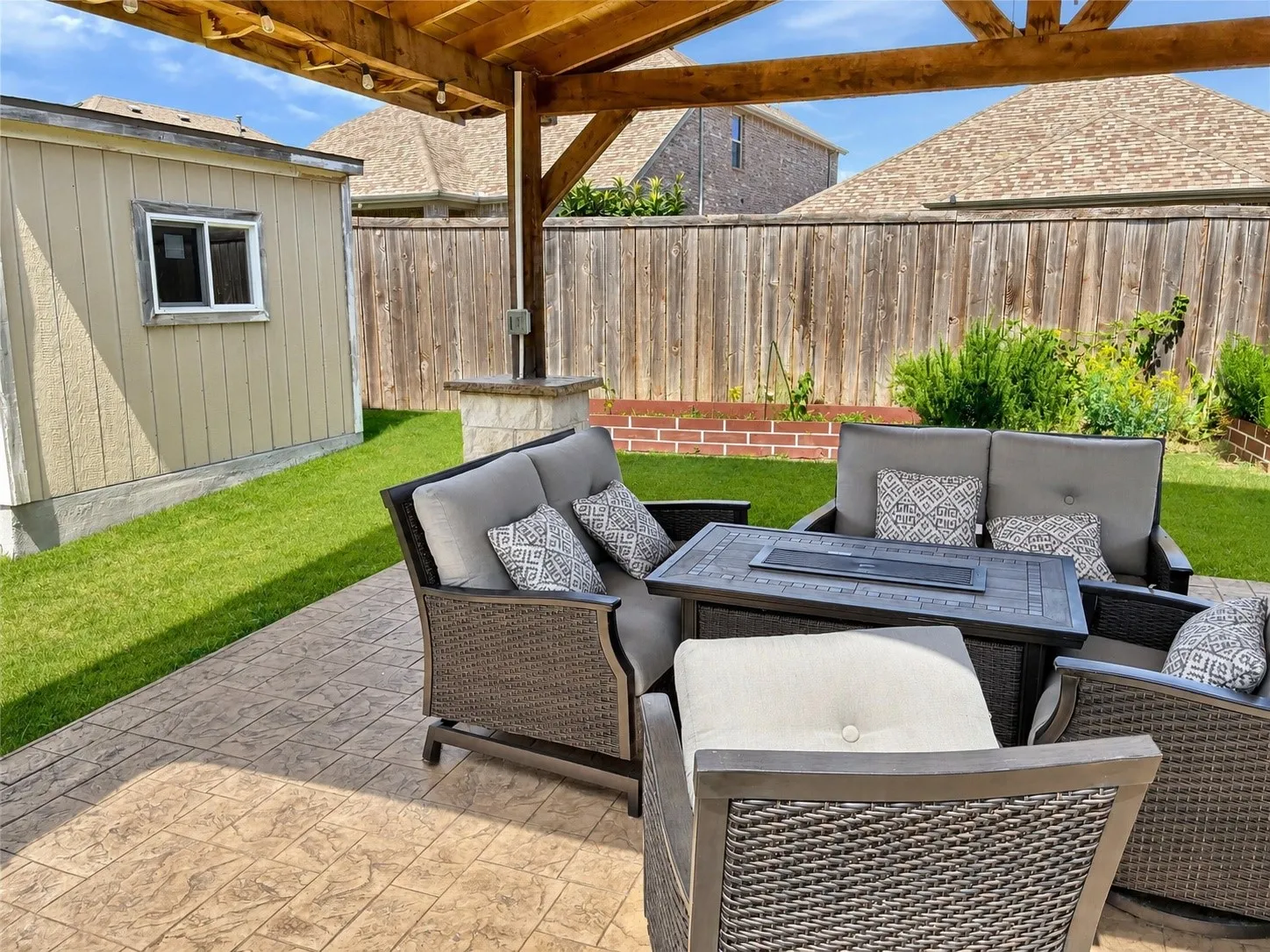 Expansive stamped concrete patio with a wooden pergola, accompanied by a detached storage building with a window