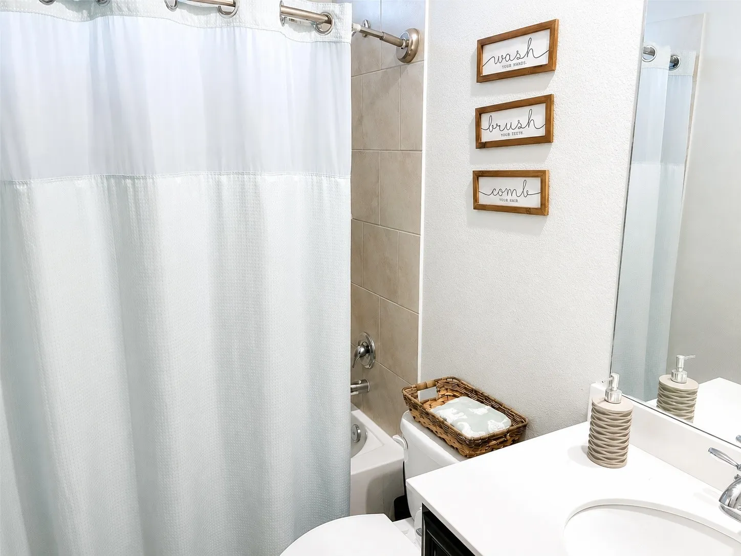 Bathroom featuring a white vanity with an integrated sink, a large wall mirror, and a tiled shower-tub combination