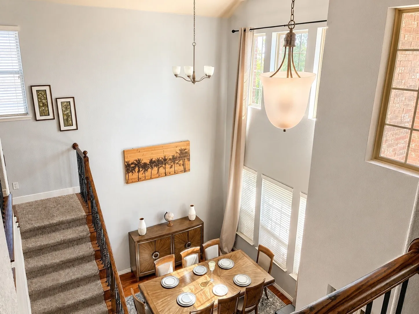Two-story interior with a dining area featuring wood-finish flooring, a contemporary chandelier, and tall windows with blinds