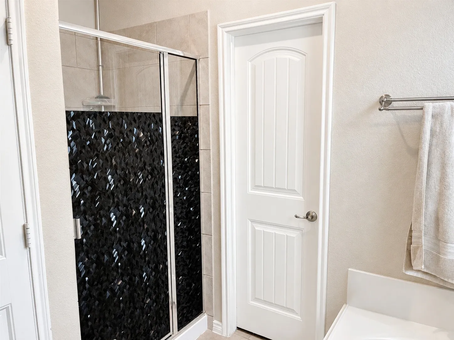 Shower enclosure featuring dark, textured wall tiling and a chrome shower head