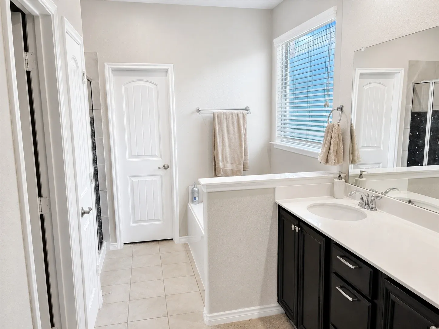 Bathroom featuring a dark wood vanity with a white countertop and undermount sink, a large wall mirror, and a window with blinds