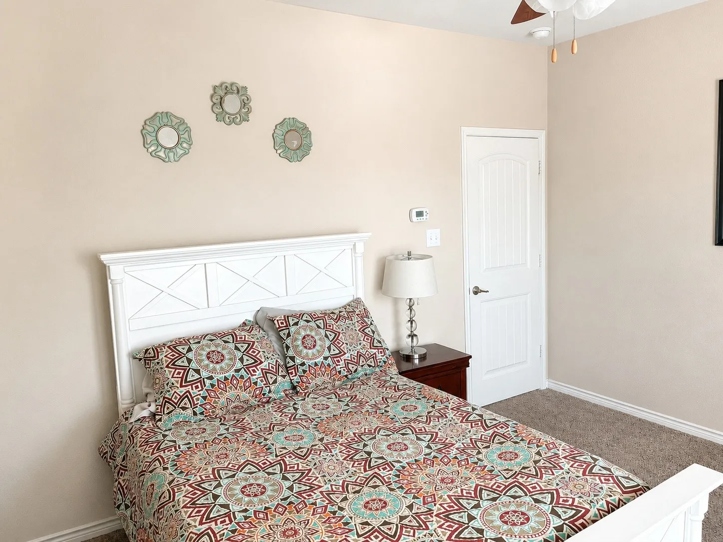 Carpeted bedroom featuring a white paneled headboard, neutral wall paint, and a white ceiling fan