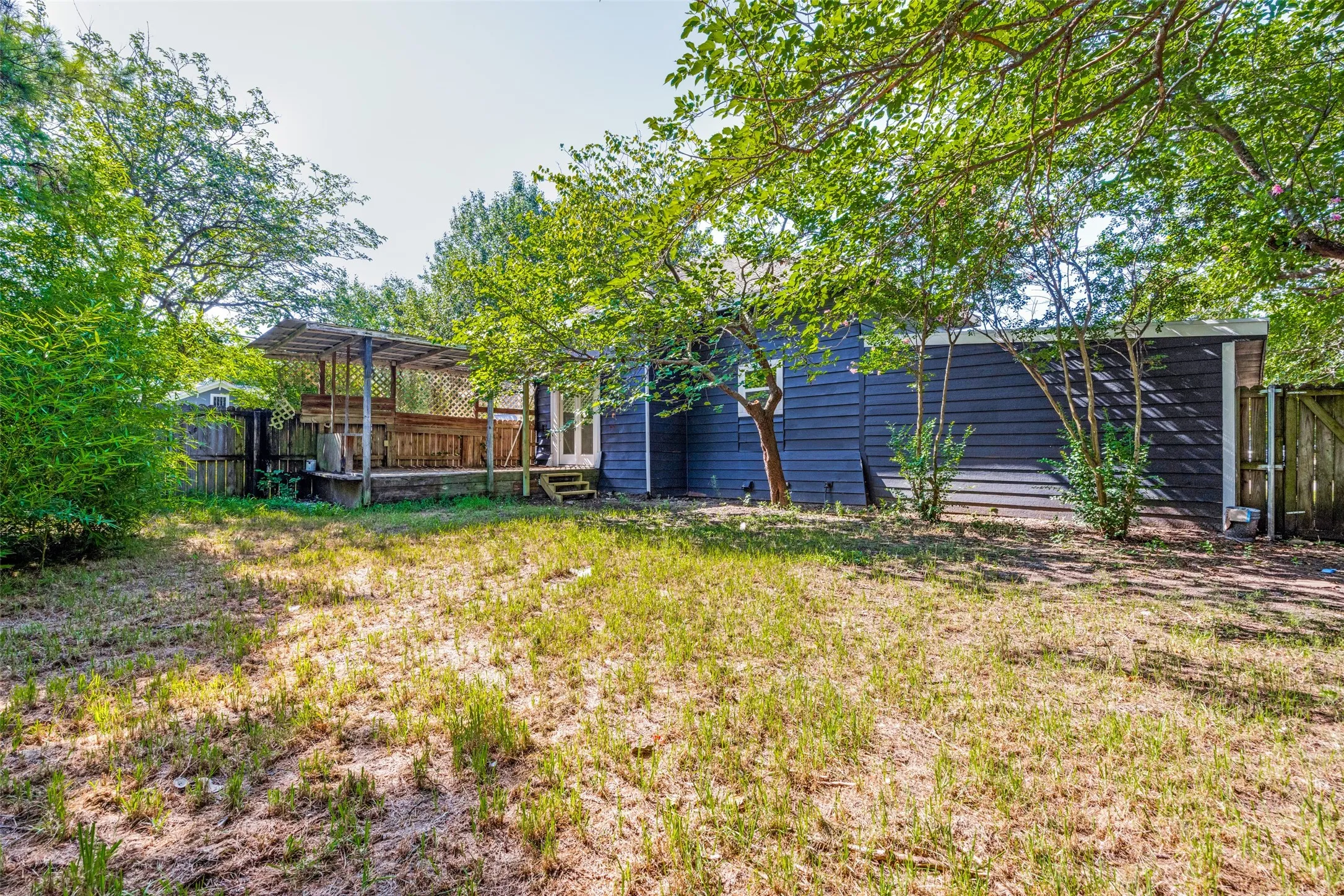 Spacious backyard featuring a covered wood deck, mature trees, and privacy fencing