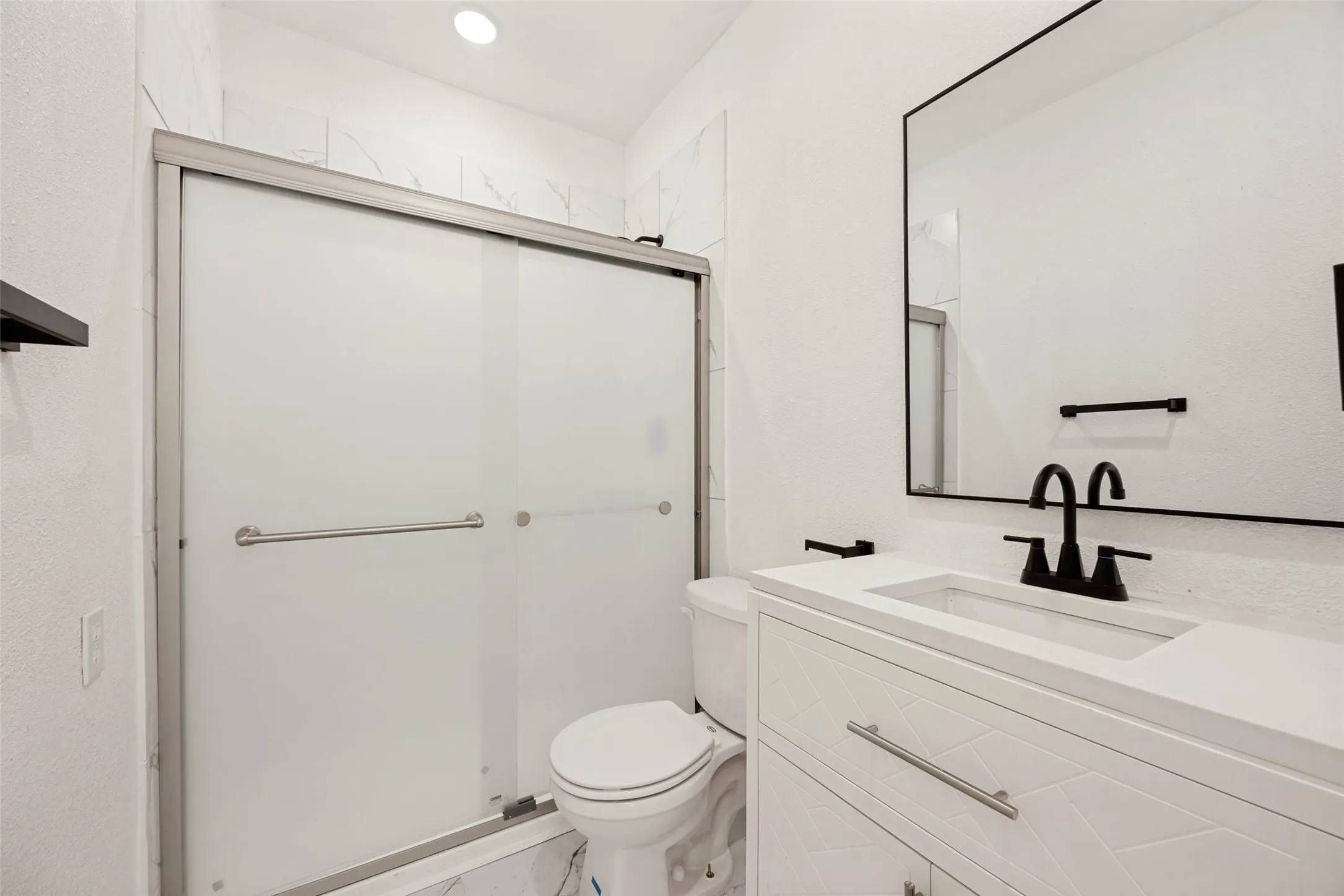 Bathroom featuring a frosted glass shower enclosure, white vanity with a rectangular sink, black framed mirror, and matte black plumbing fixtures