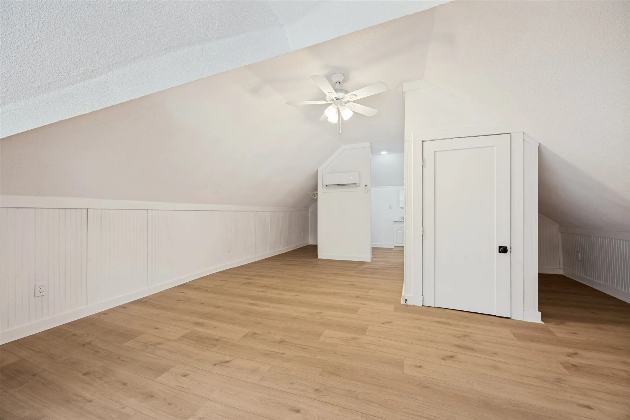 Attic space featuring wood-finish flooring, white beadboard paneling, and a ceiling fan
