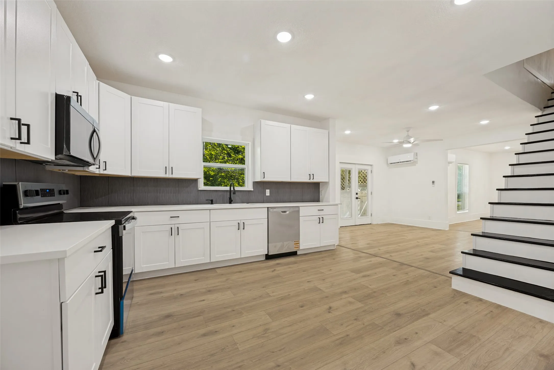 Modern kitchen featuring white shaker cabinetry, stainless steel appliances, a dark subway tile backsplash, and light wood-finish flooring