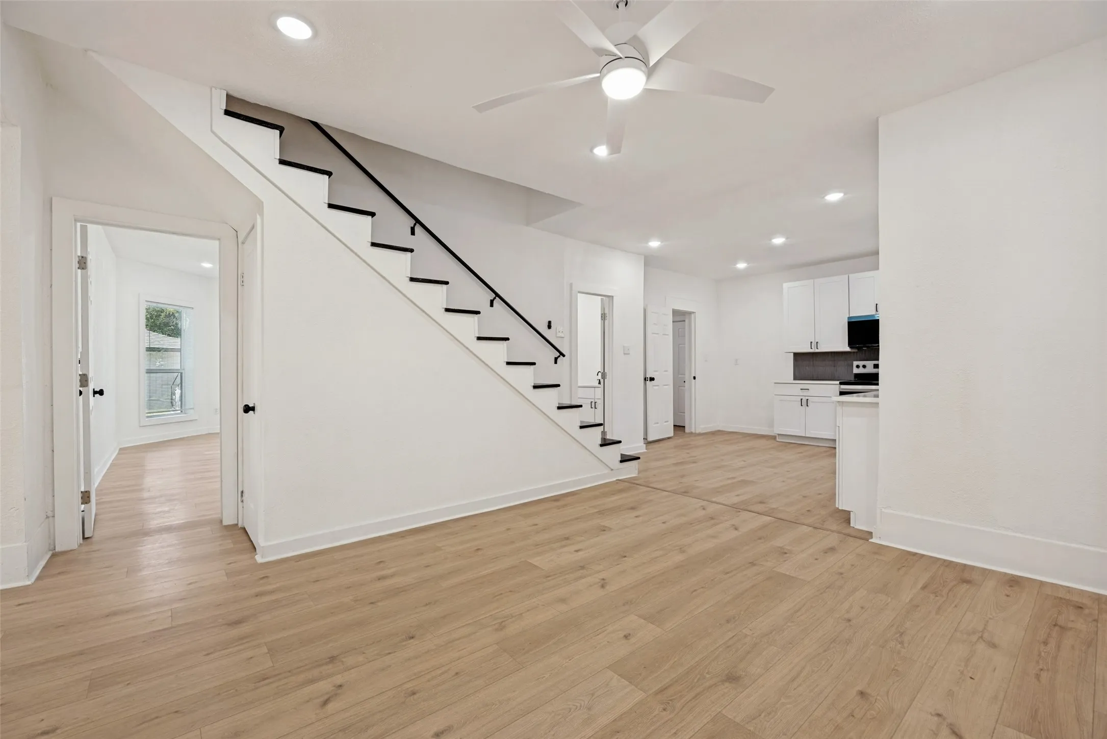 Open-concept living space featuring wood-finish flooring, recessed lighting, and a modern staircase with black railing