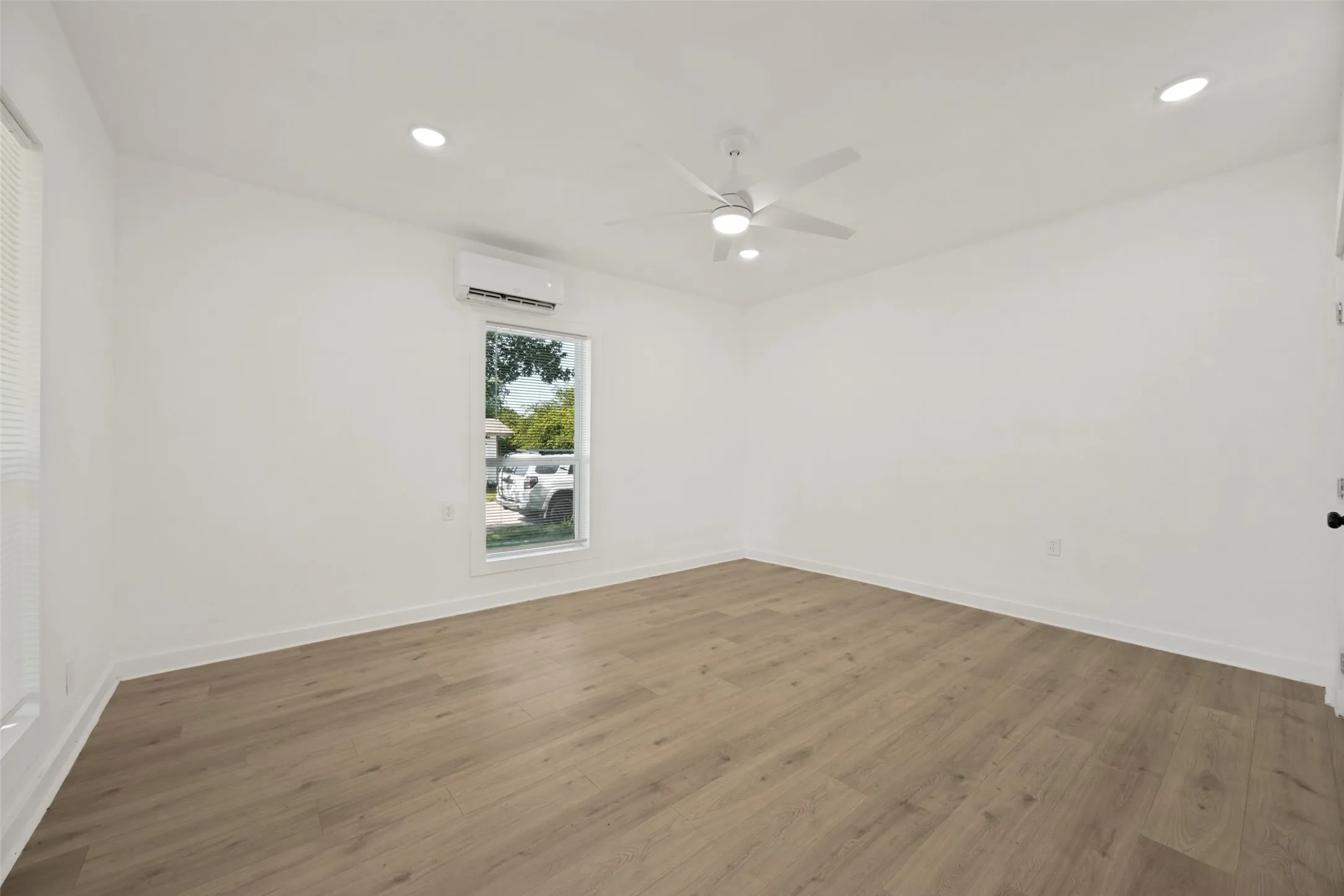 Spacious room featuring light wood-finish flooring, recessed lighting, and a white ceiling fan