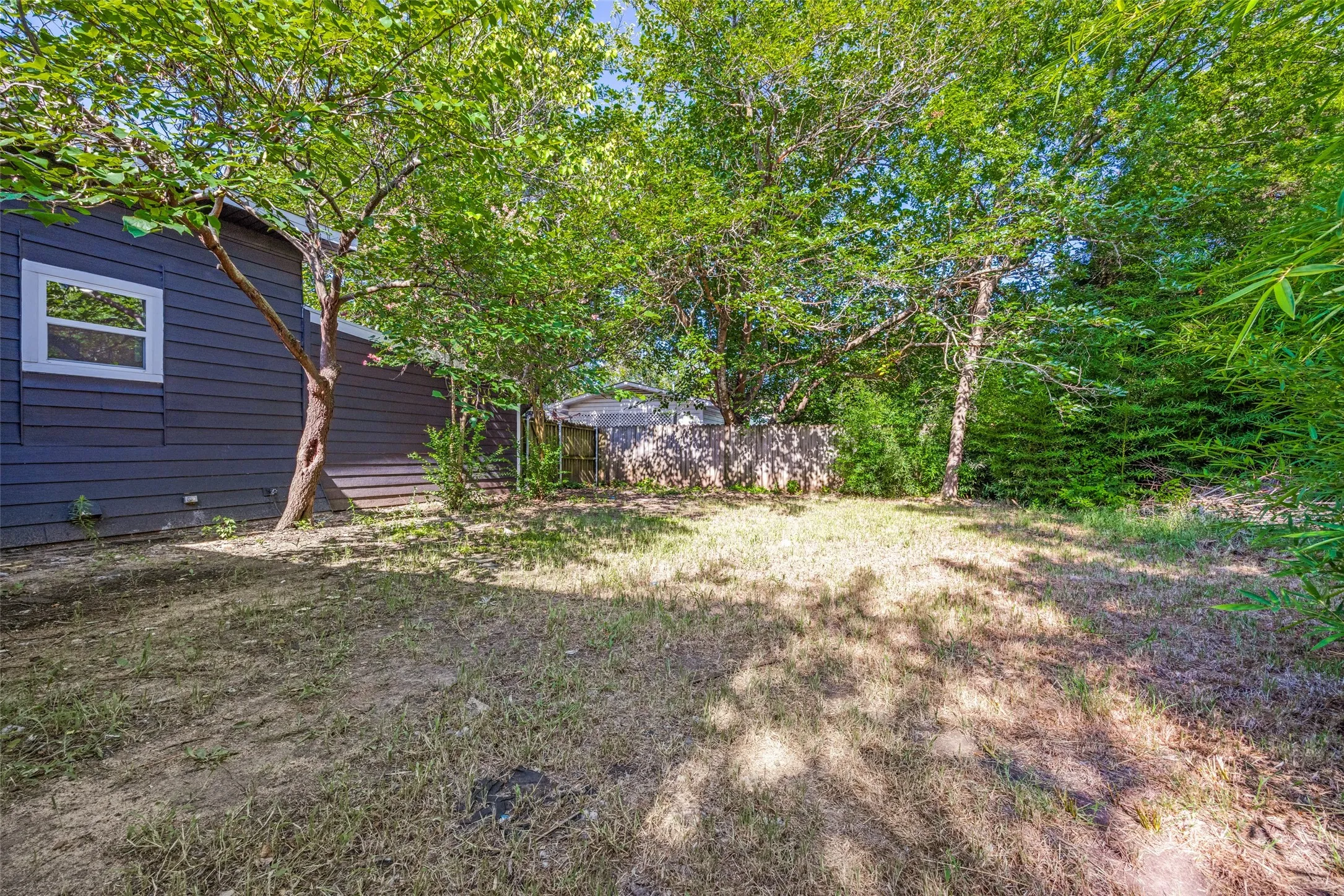 Spacious backyard with mature shade trees, a privacy fence, and a dark-colored siding exterior