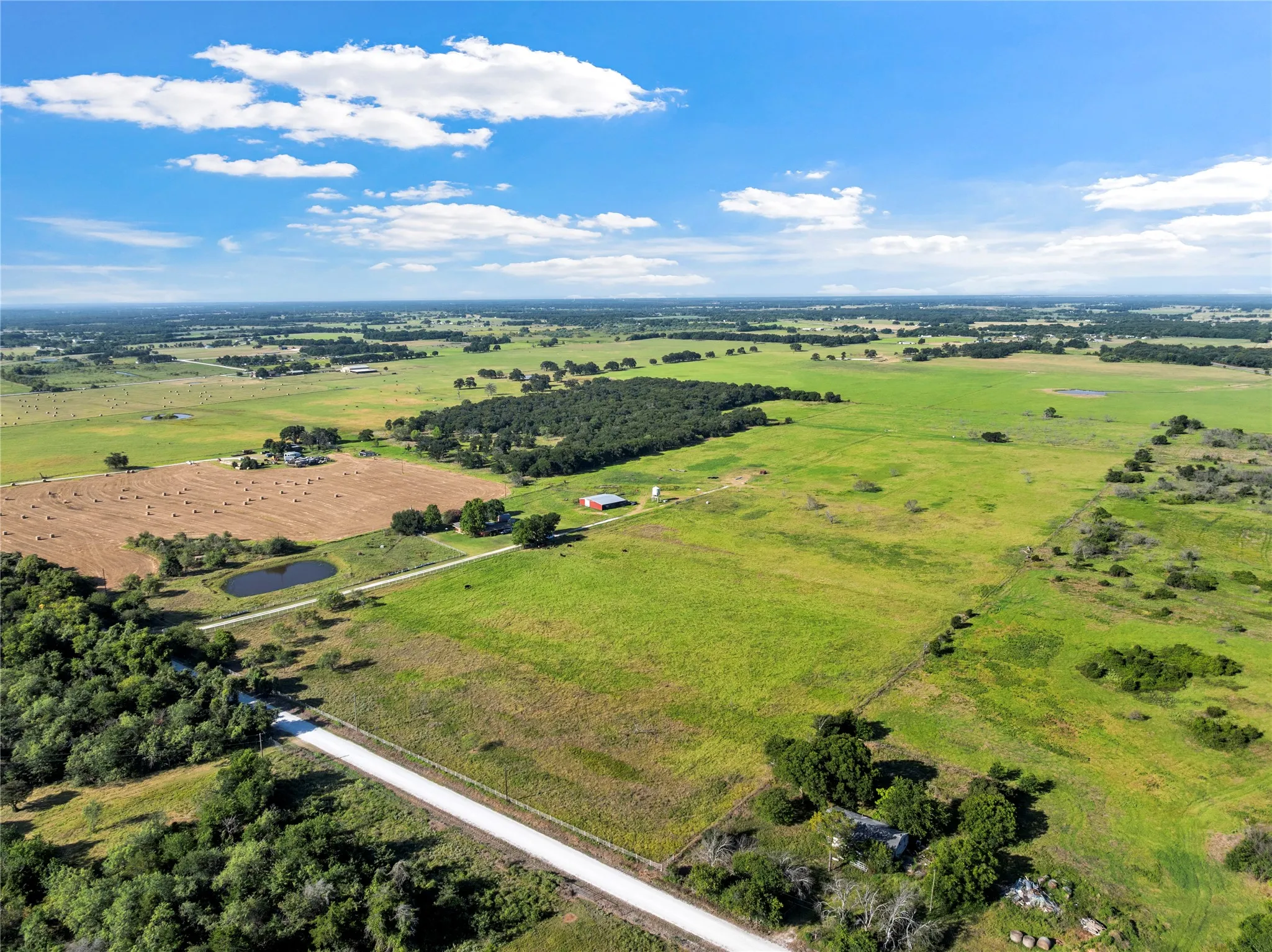 Expansive rural landscape featuring extensive green pastures and a visible pond