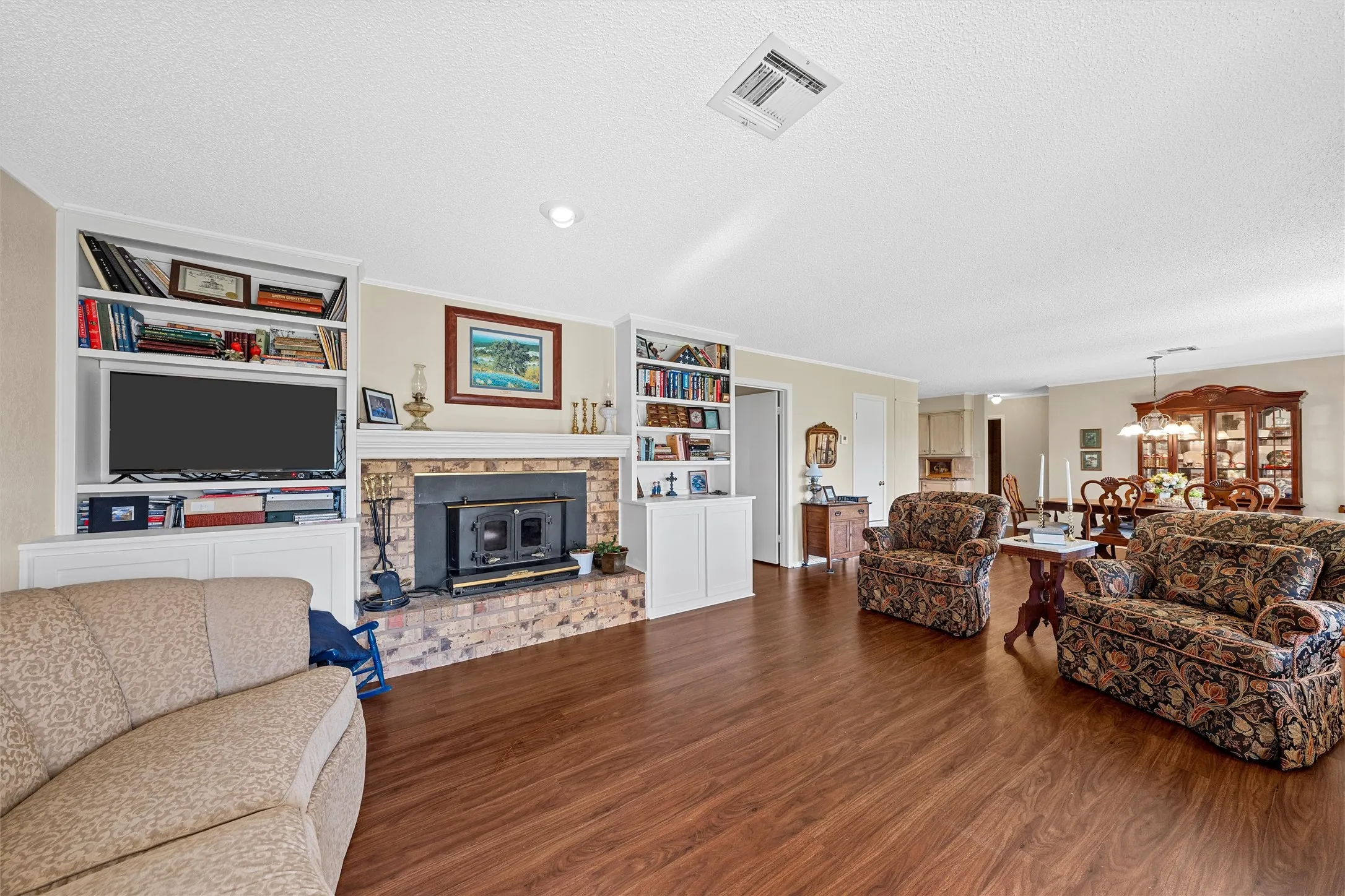 Spacious living area featuring wood-finish flooring, a brick fireplace with a wood-burning insert, and custom built-in shelving