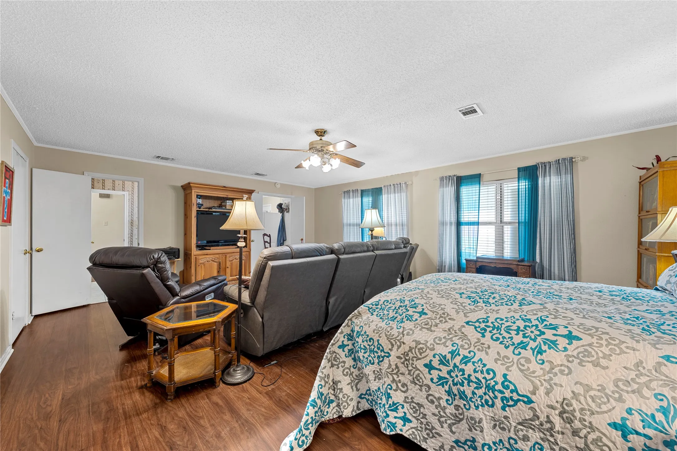 Spacious room featuring wood-finish flooring, light-colored wall paint, multiple windows with blinds, a ceiling fan with integrated lighting, and white trim