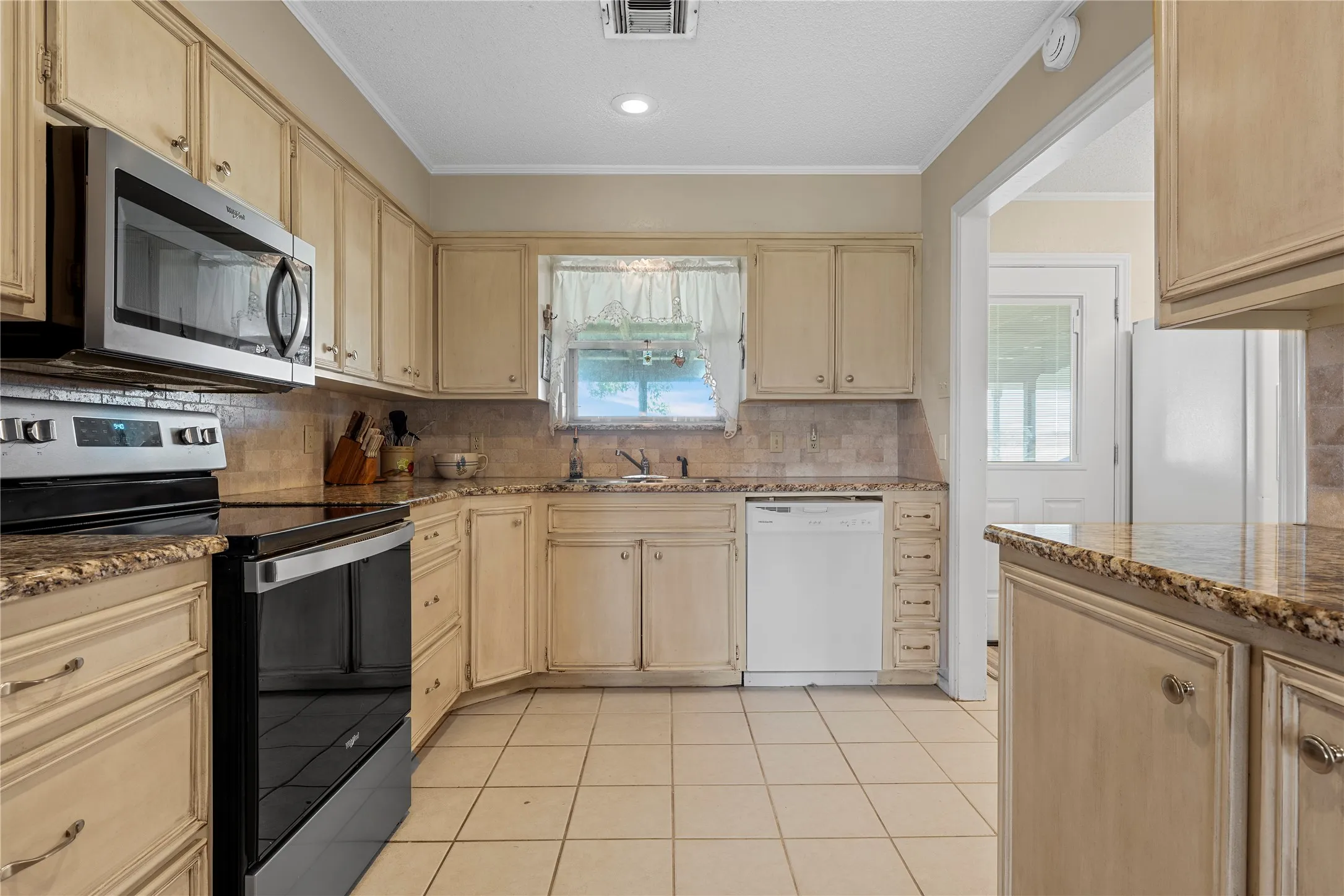 Kitchen featuring tile flooring, light-toned cabinetry, a stainless steel microwave, a black electric range, and solid surface countertops with a tile backsplash