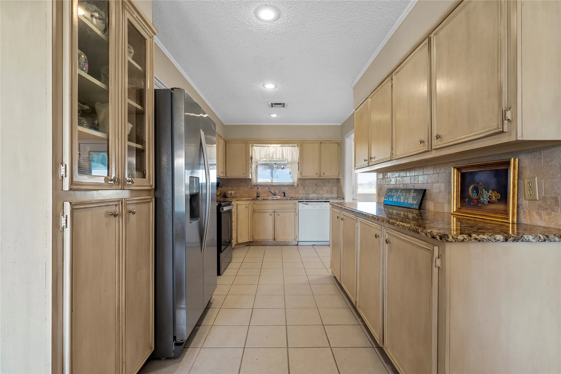 Kitchen featuring extensive cabinetry with some glass-front uppers, granite-style countertops, tile backsplash, and recessed lighting