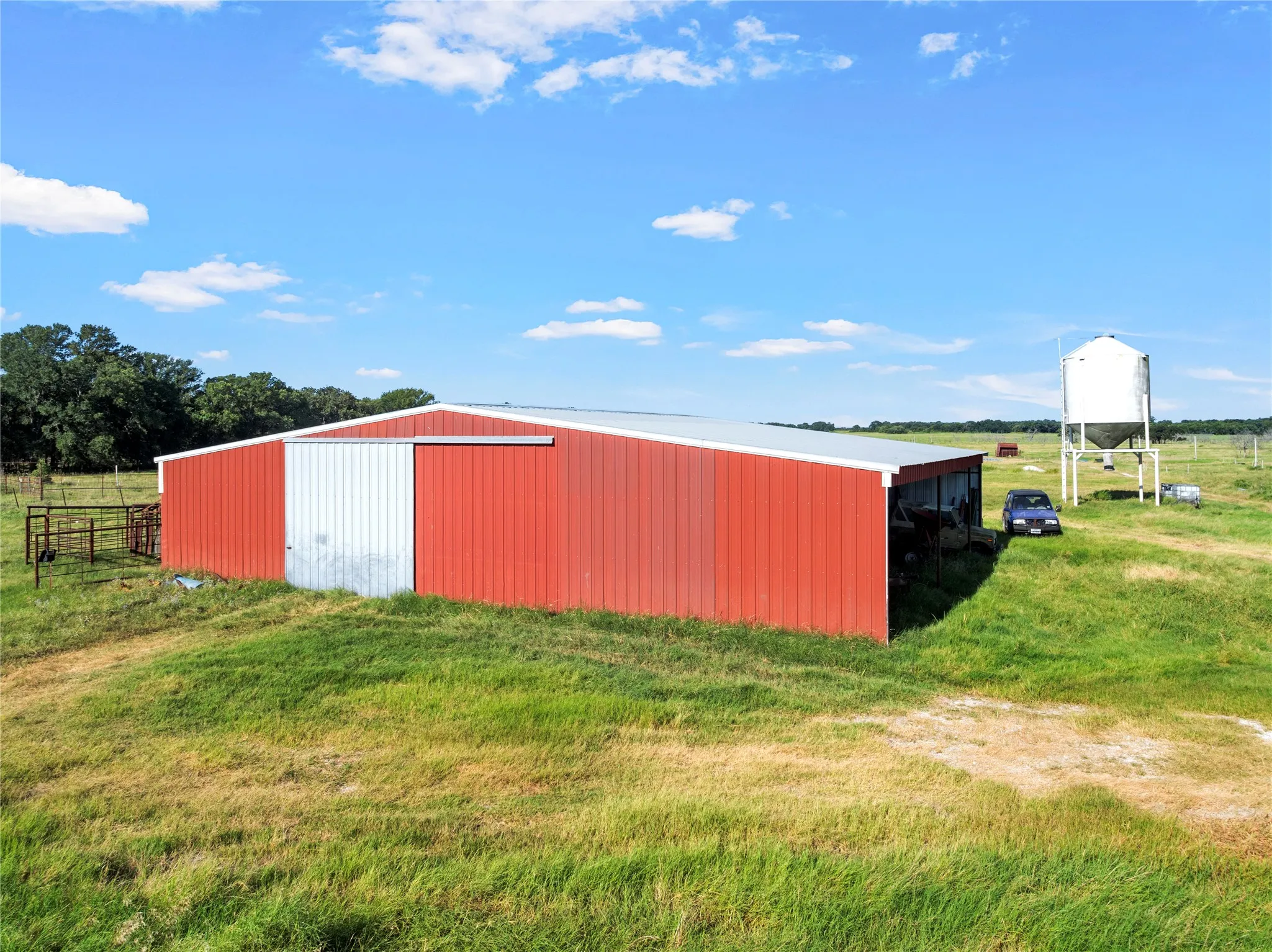 Red metal barn with a sliding metal door and a white metal roof, situated on a grassy expanse with a distant water tower