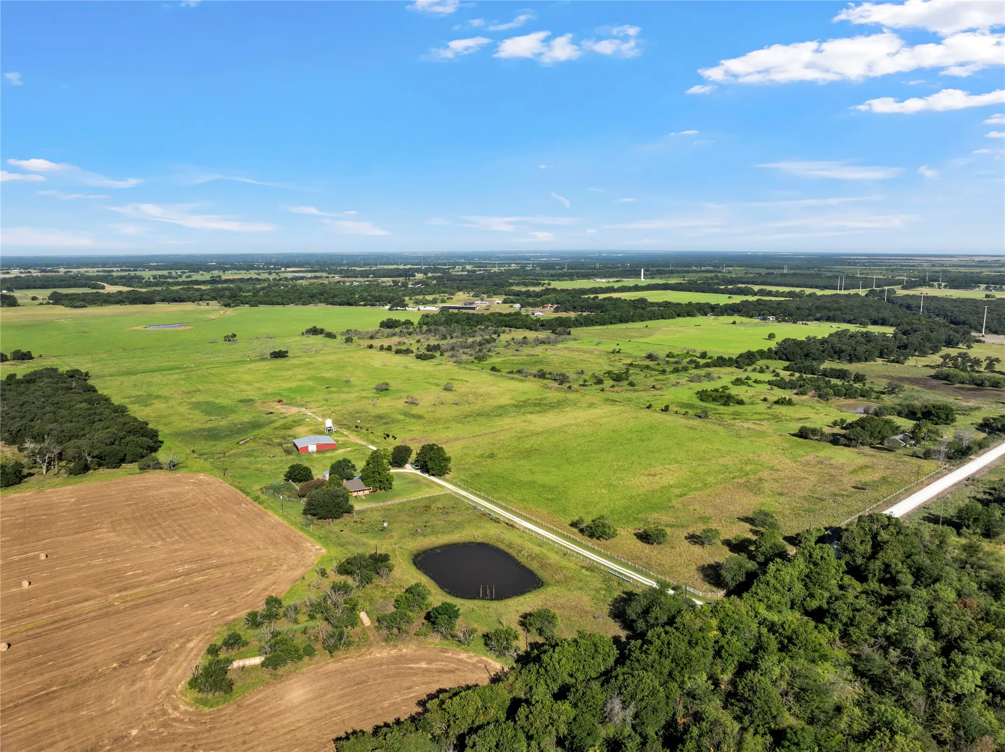 Expansive rural property featuring a main residence, additional red barn structure, private pond, and extensive green pastures