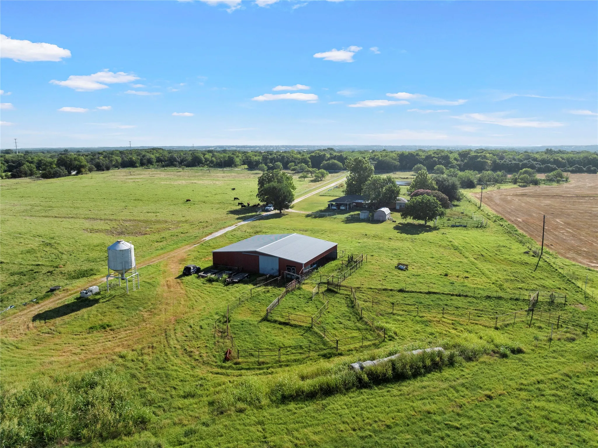 Expansive rural property featuring an agricultural building with a metal roof, a water tower, and a residence set amidst mature trees