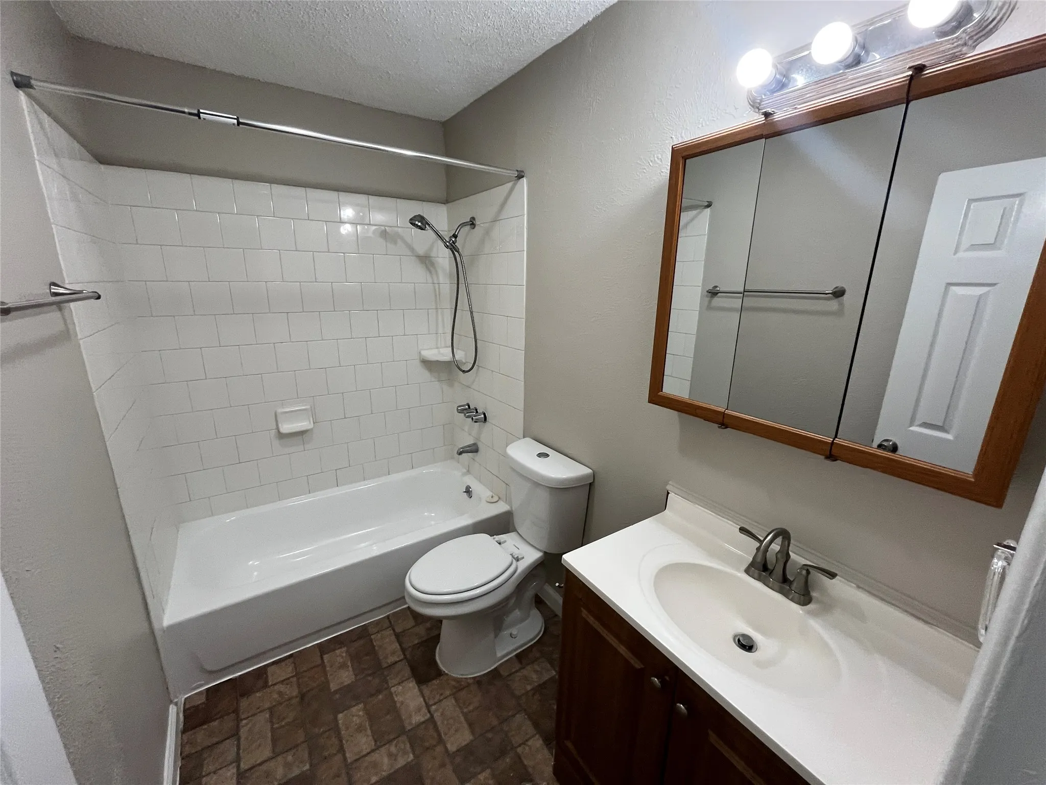Bathroom featuring a white bathtub, subway tile surround, wood-finish vanity with a white countertop, and a mirrored medicine cabinet