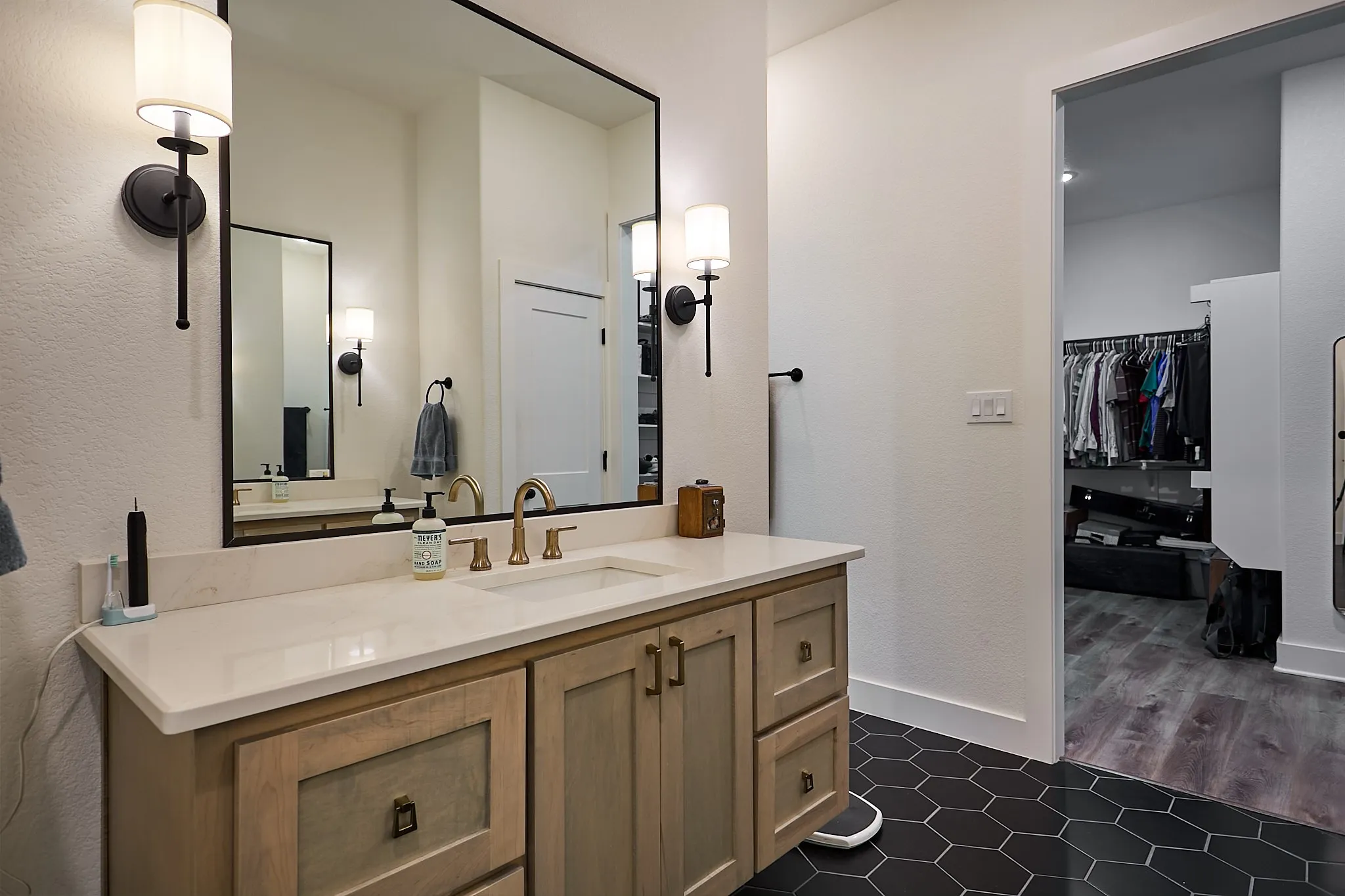 Vanity area featuring a large rectangular mirror, dual sconce lighting, and a light-toned wood-finish vanity with a light countertop