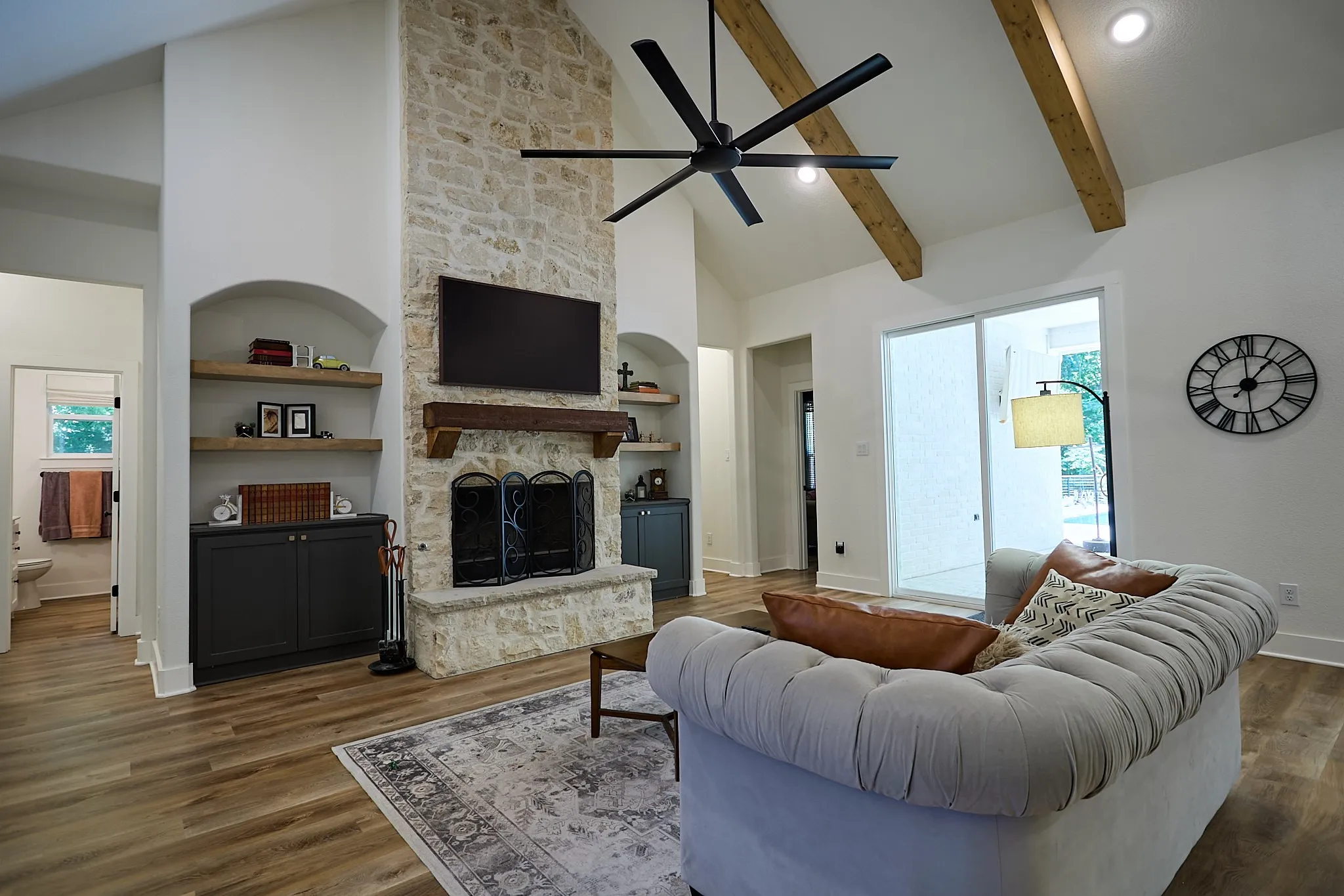 Living area featuring a stone-clad fireplace with wood mantle, vaulted ceiling with exposed wood beams, wood-finish flooring, recessed lighting, and sliding glass doors