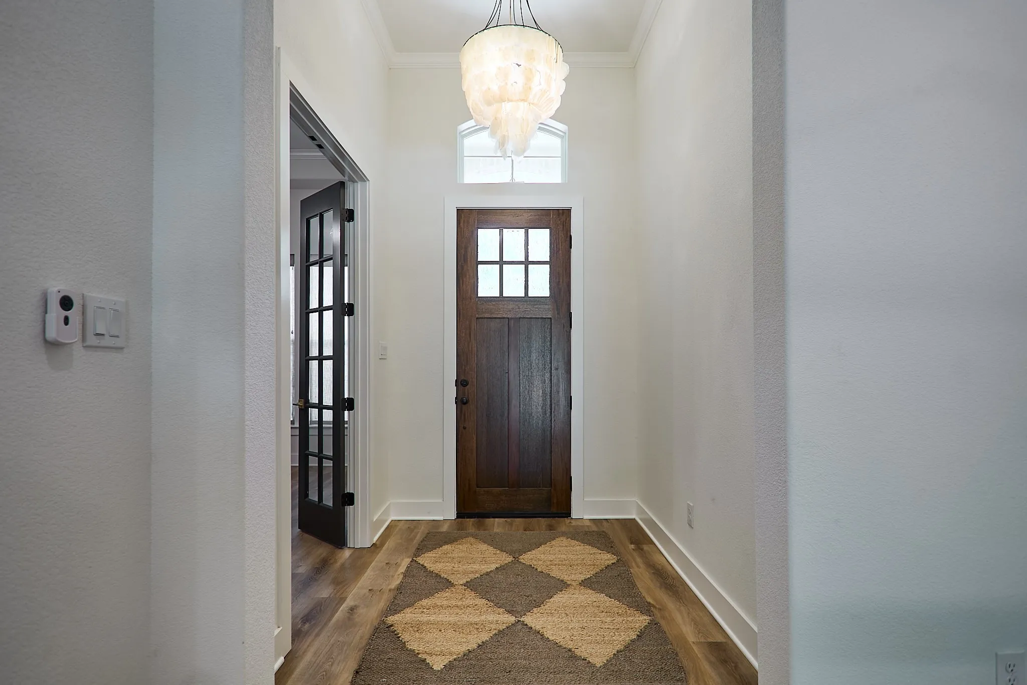 Entryway featuring a dark wood-finish door with glass panels, an arched transom window, and a chandelier with shell-like accents