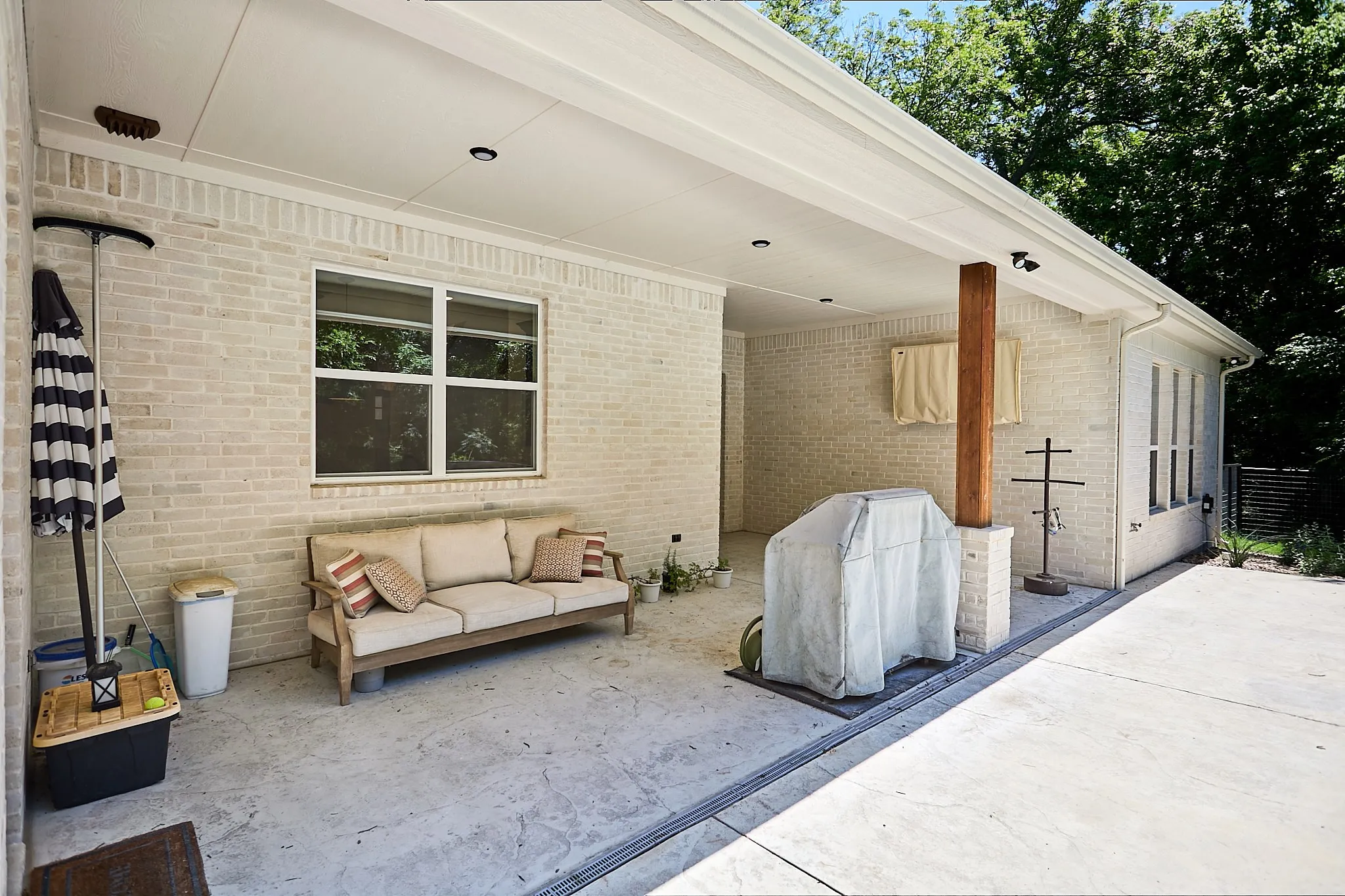 Covered patio featuring whitewashed brick, recessed lighting, concrete flooring, a natural wood support column, and multiple windows