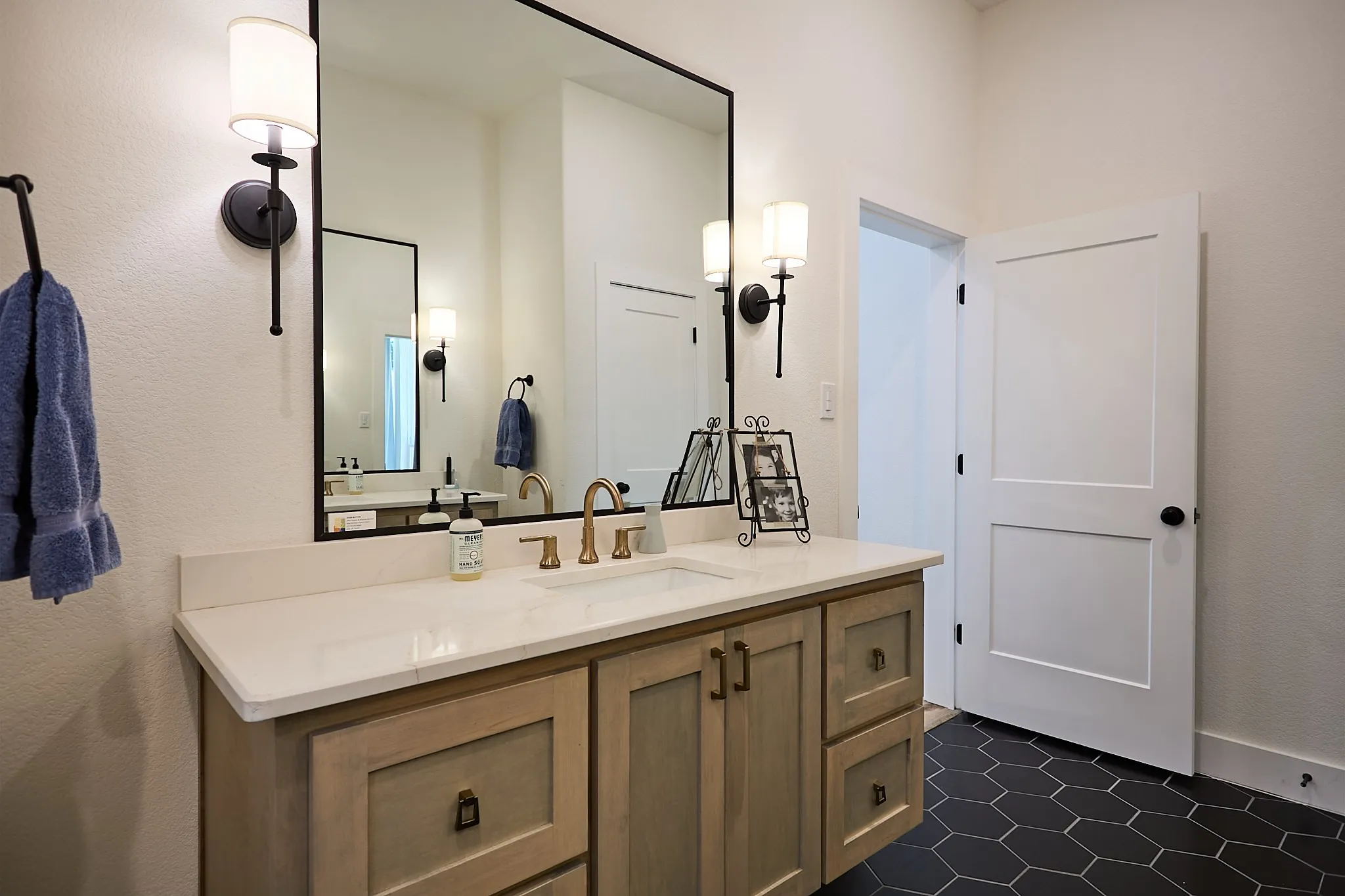 Bathroom featuring a light wood vanity with a white countertop, undermount sink, and brass-finish faucet