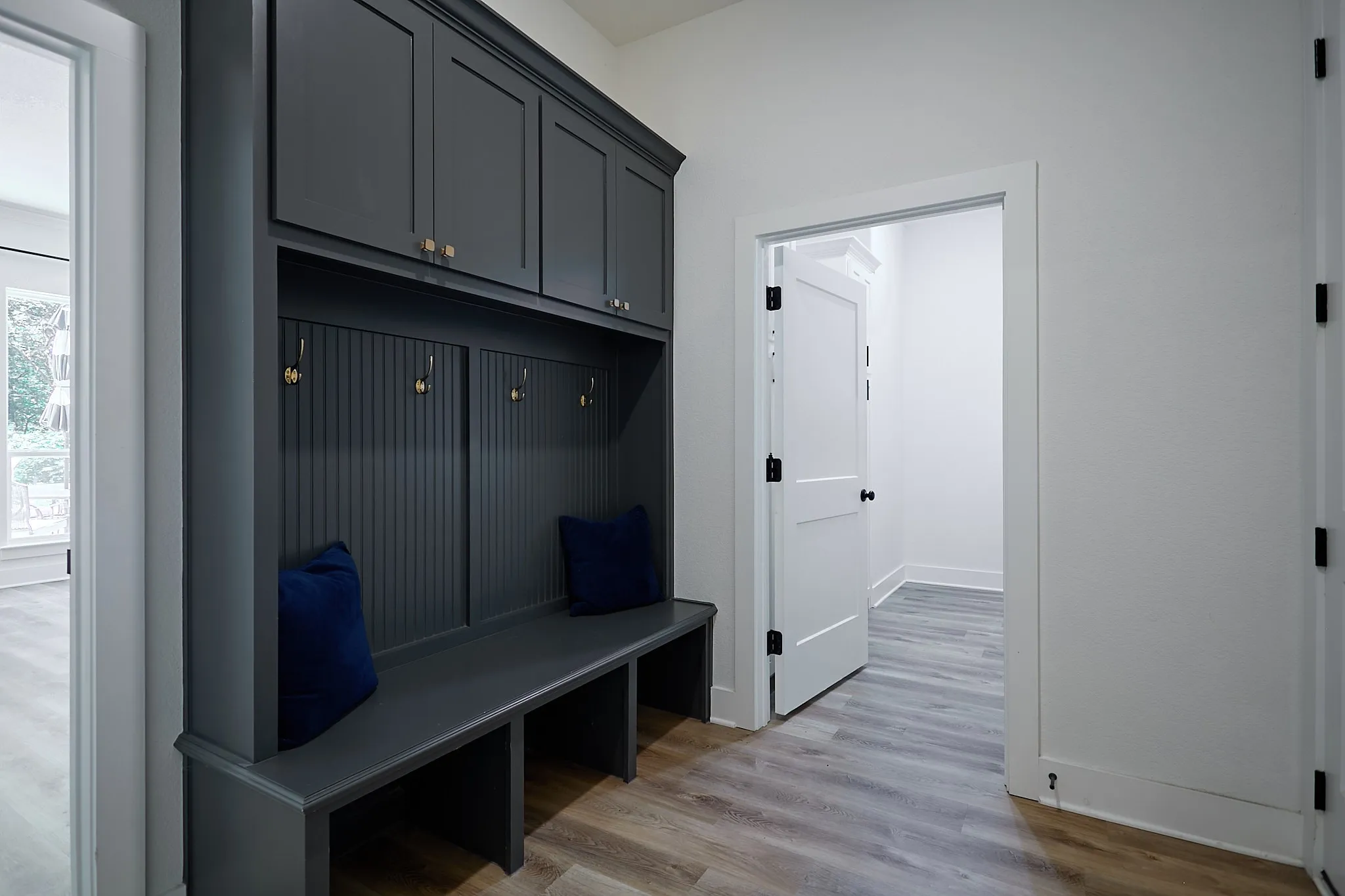 Built-in mudroom bench with overhead cabinetry and beadboard backing, featuring gold-toned hooks and hardware