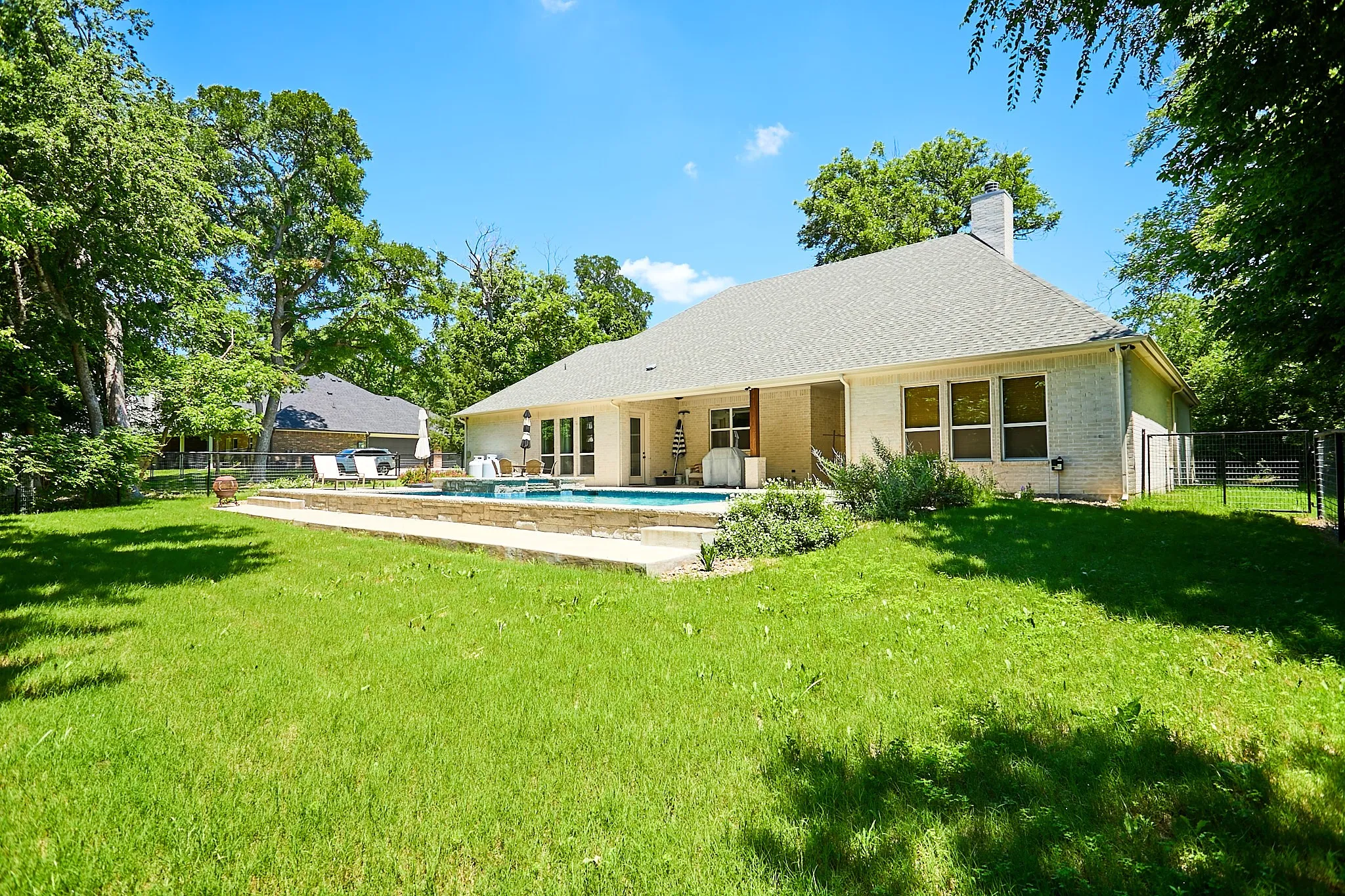 Expansive backyard featuring a rectangular swimming pool with stone surround, a paved patio area, and mature trees