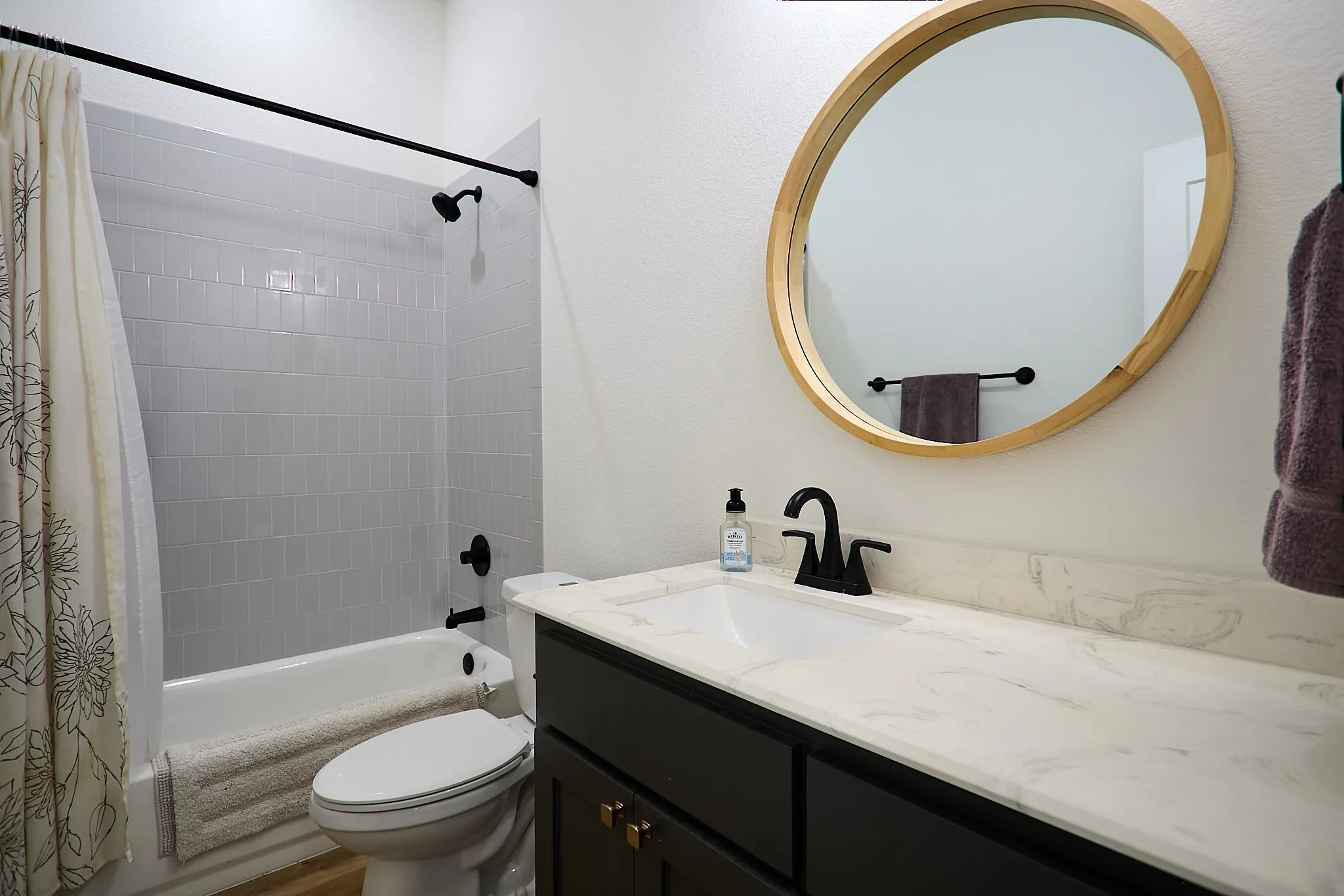 Bathroom featuring a vanity with a white countertop and integrated sink, matte black faucet, and a round wood-framed mirror