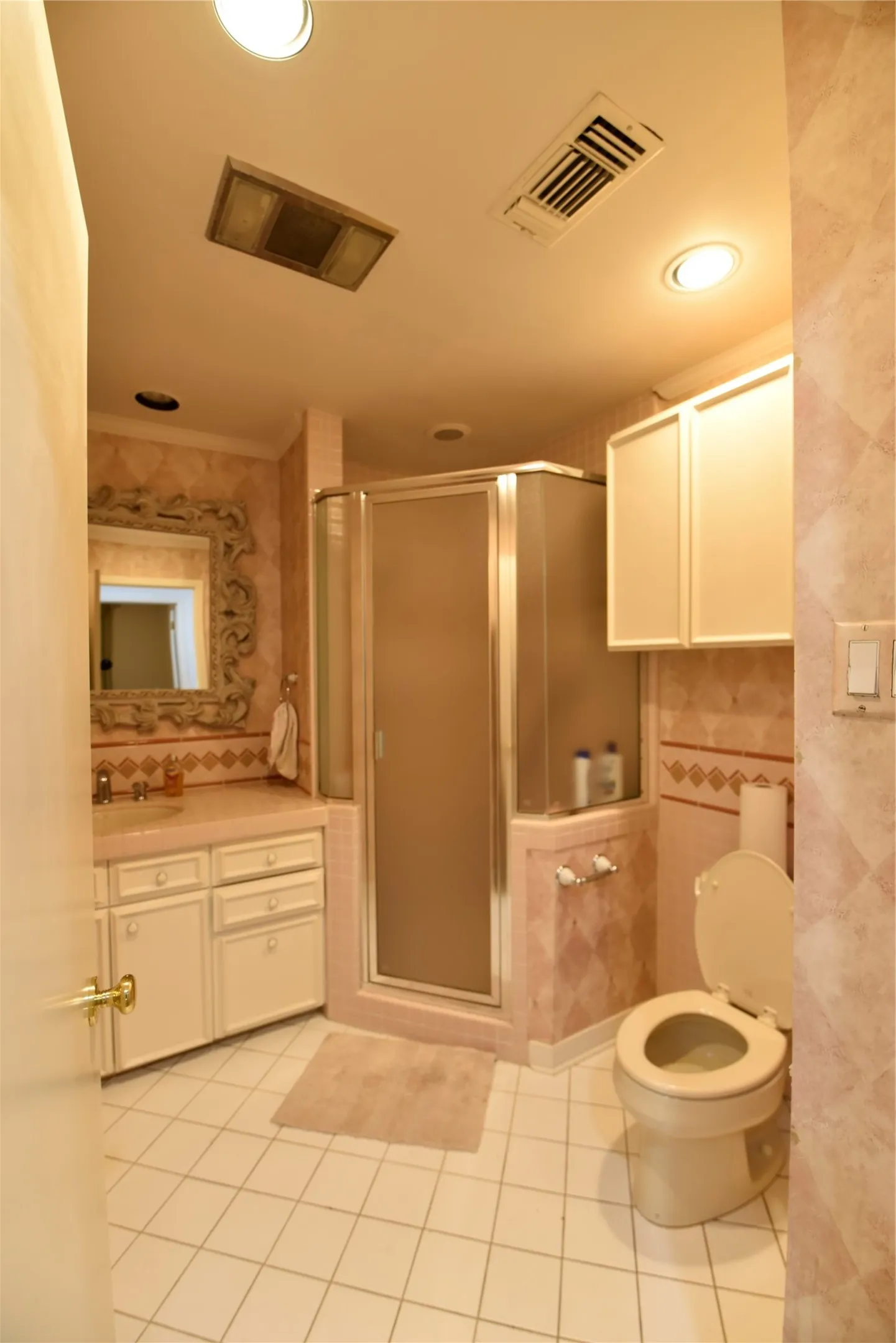 Bathroom featuring white square floor tiles, a glass-enclosed corner shower, and a vanity with a countertop sink
