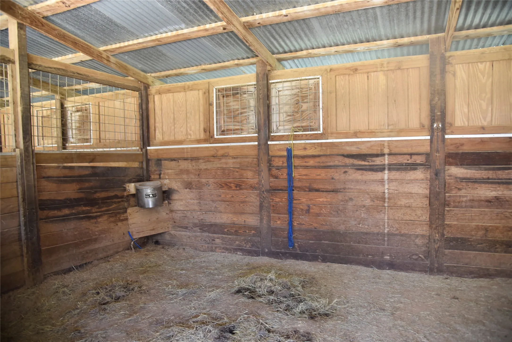 Stall interior featuring wood plank walls, corrugated metal roofing, exposed wood beams, and an integrated feeding trough