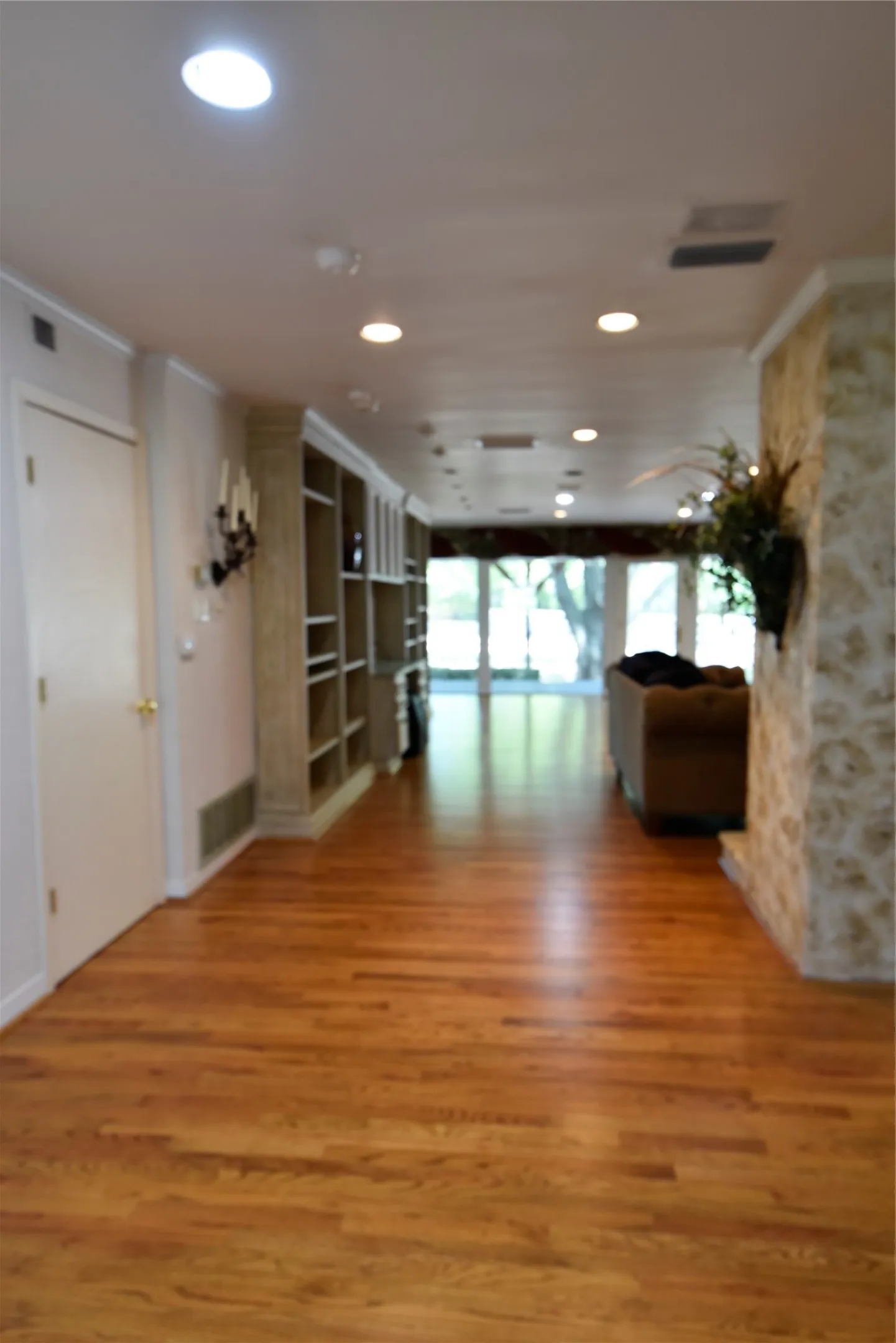 Hardwood flooring extending through a spacious interior with recessed lighting, built-in shelving, and a stone-clad wall feature