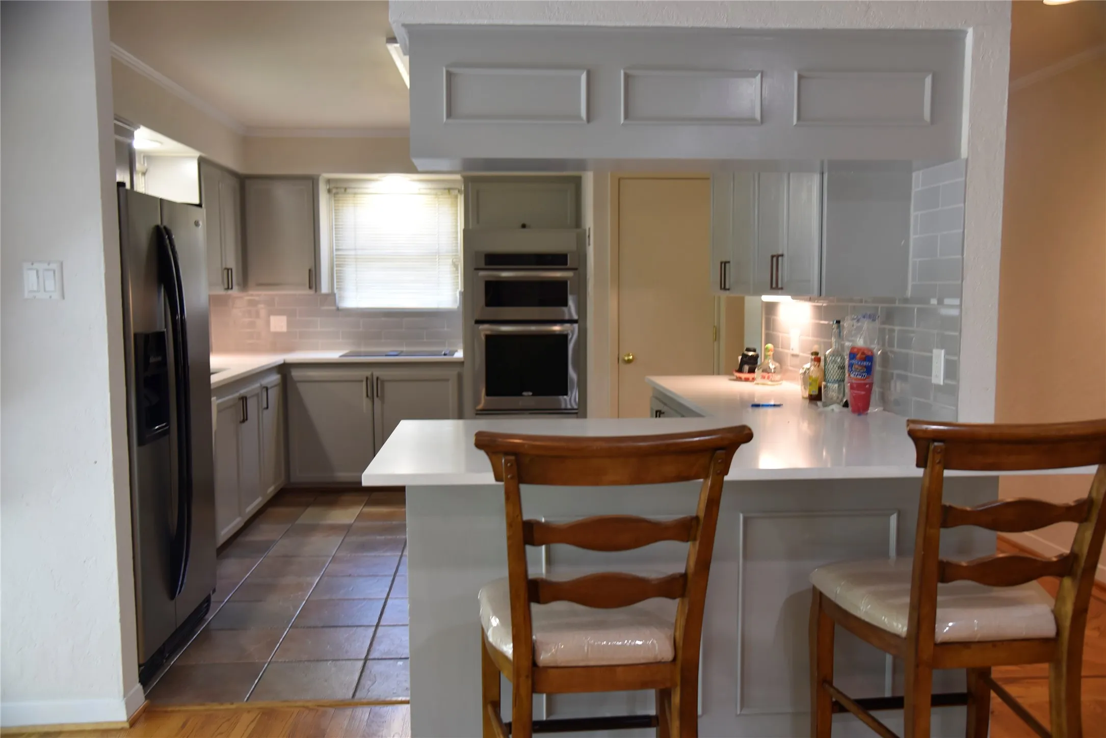 Updated kitchen featuring light gray cabinetry, stainless steel appliances, a white solid surface countertop, and a gray subway tile backsplash