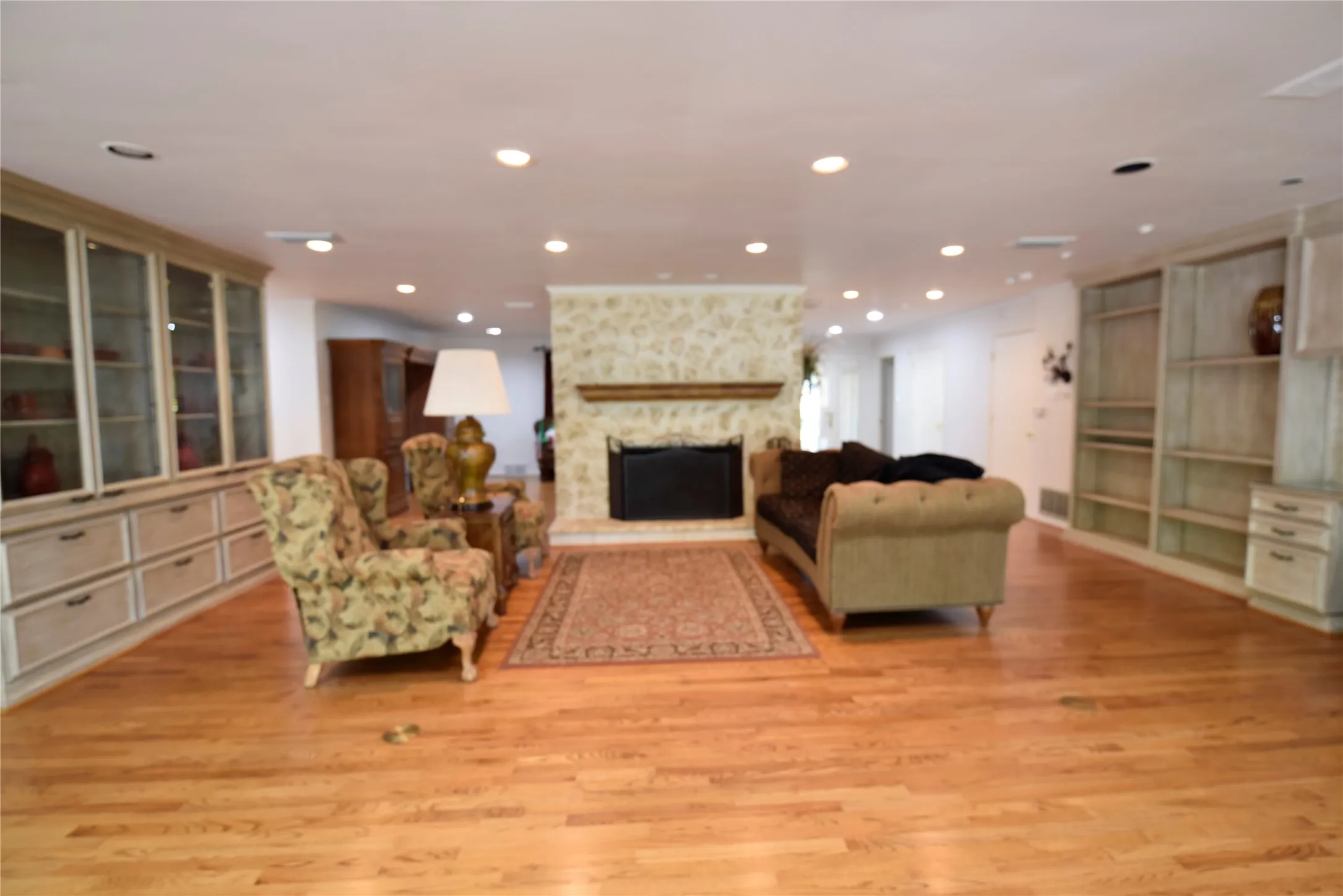 Living area featuring a stone-clad fireplace with wood mantle, built-in display cabinetry, recessed lighting, and wood-finish flooring