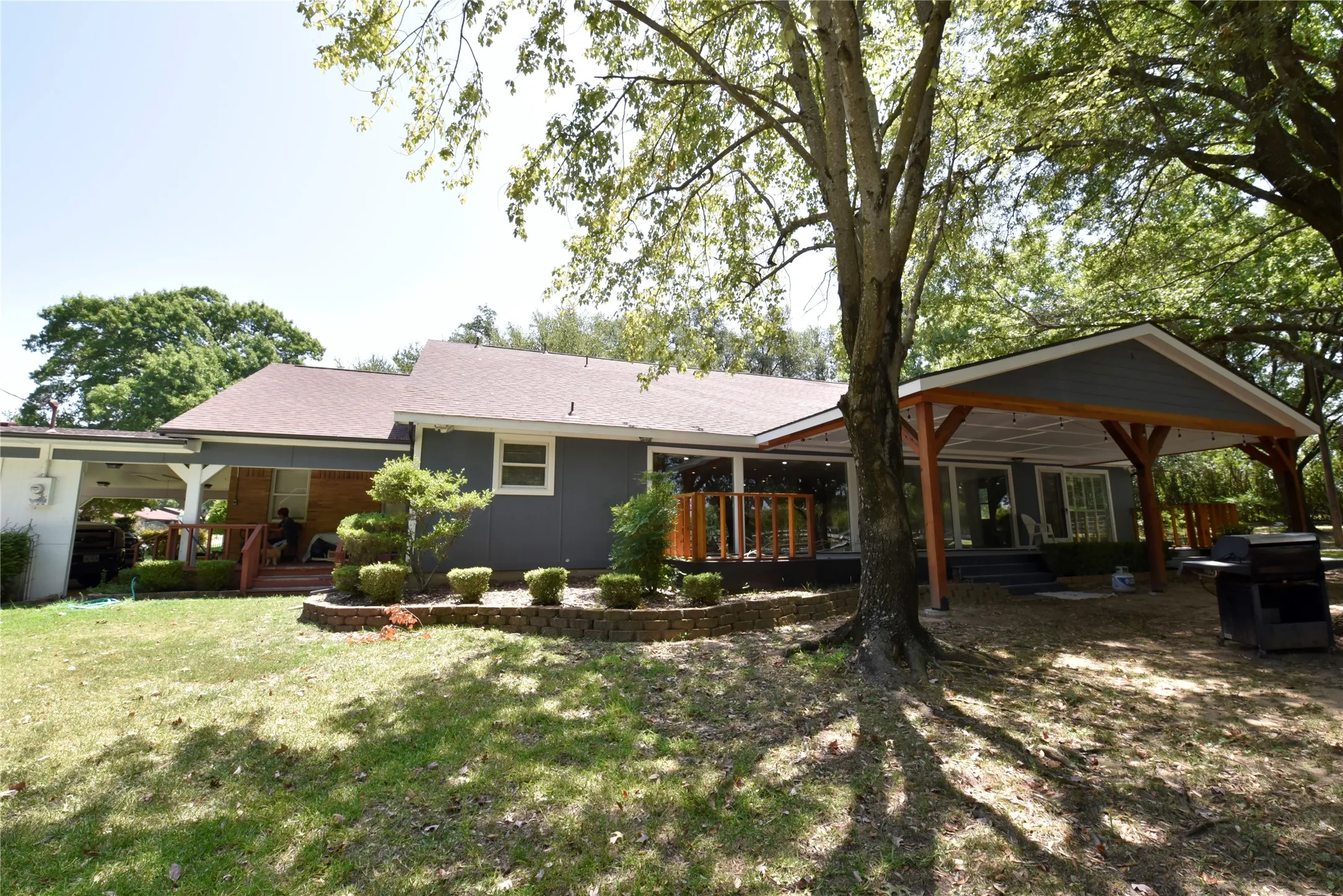 Rear exterior featuring a covered patio with exposed wood beams, a spacious wood deck, and a detached carport