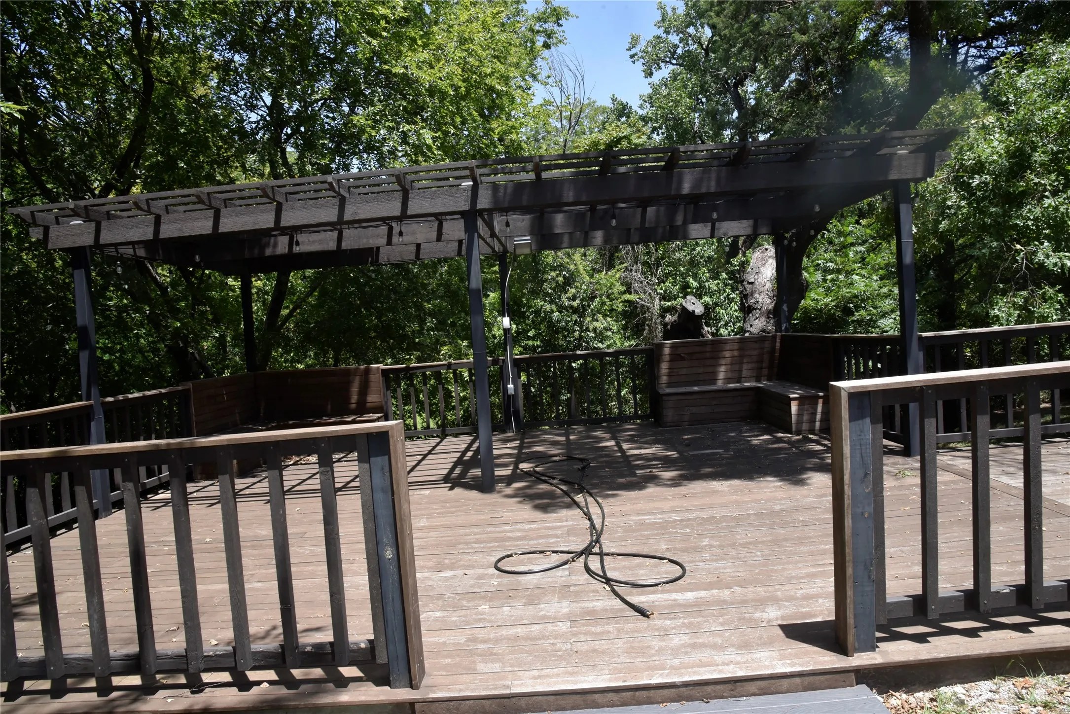 Expansive outdoor deck featuring a dark-stained wood pergola, integrated bench seating, and wood railing