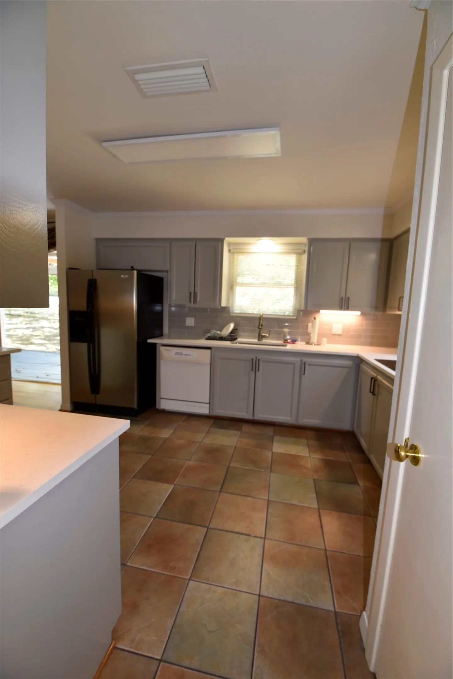 Kitchen featuring light gray cabinetry, a stainless steel refrigerator, white dishwasher, tile backsplash, and multi-toned square tile flooring